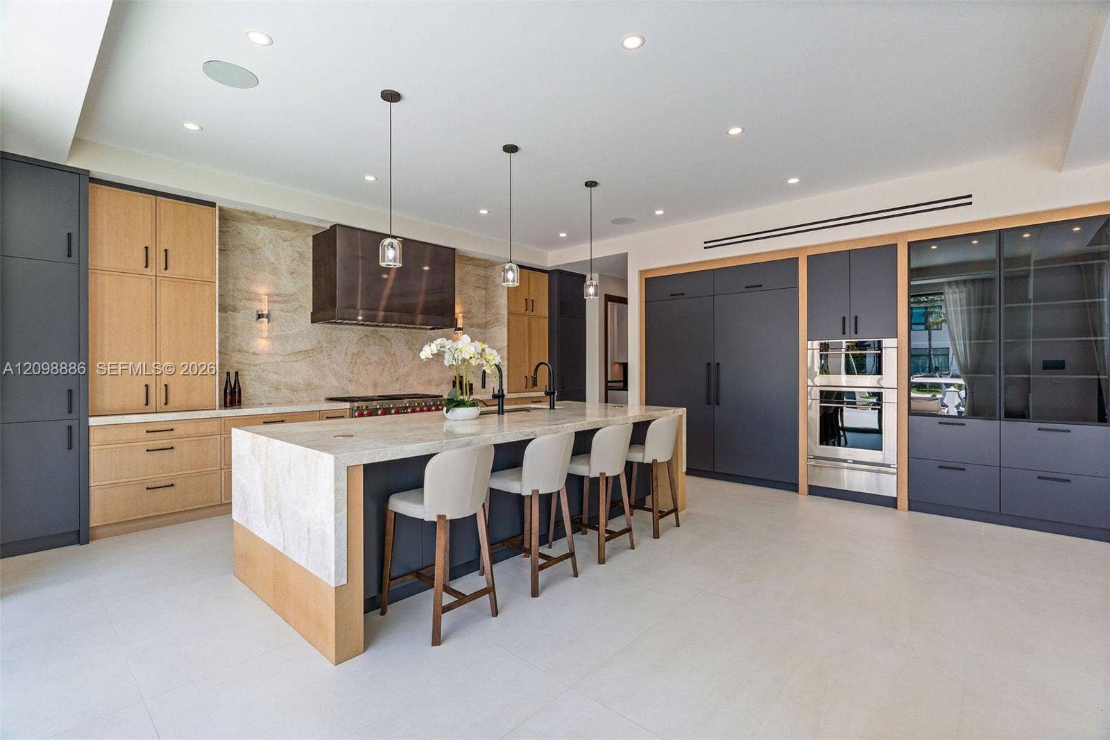 Kitchen featuring custom two-tone cabinetry, expansive stone-topped central island, built-in stainless steel double ovens, integrated refrigerator, and full-height stone backsplash