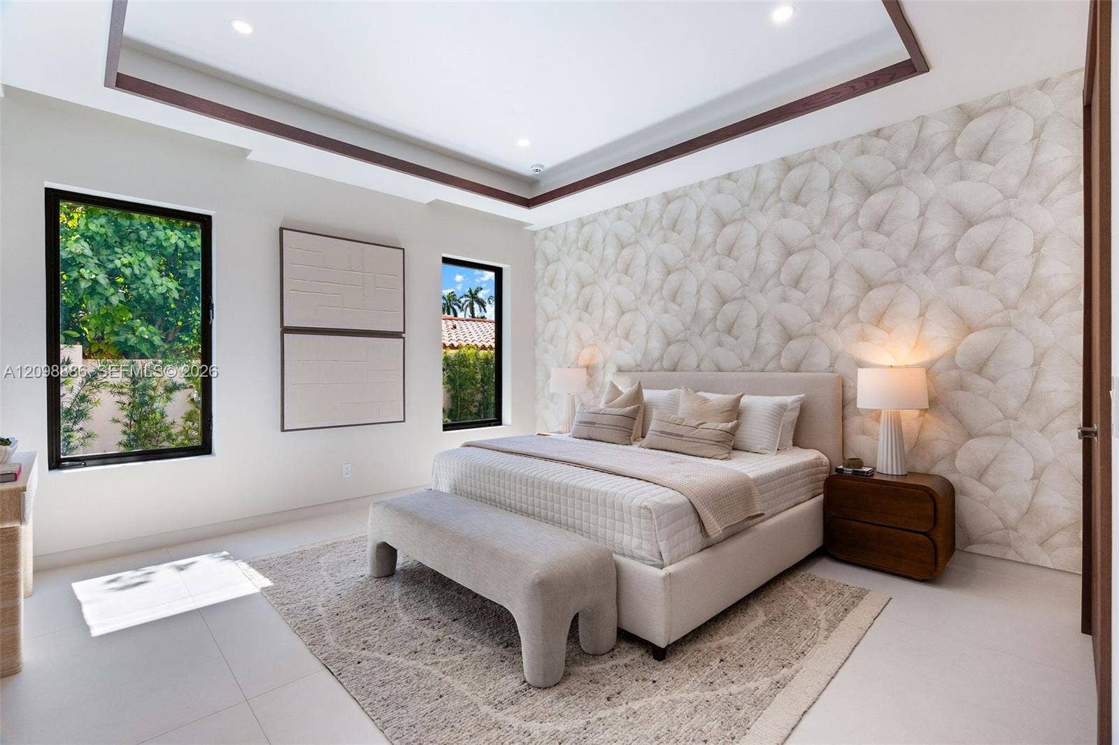 Tray ceiling with dark wood-finish trim, patterned wallpaper accent wall, large picture windows with black frames, and neutral tile flooring