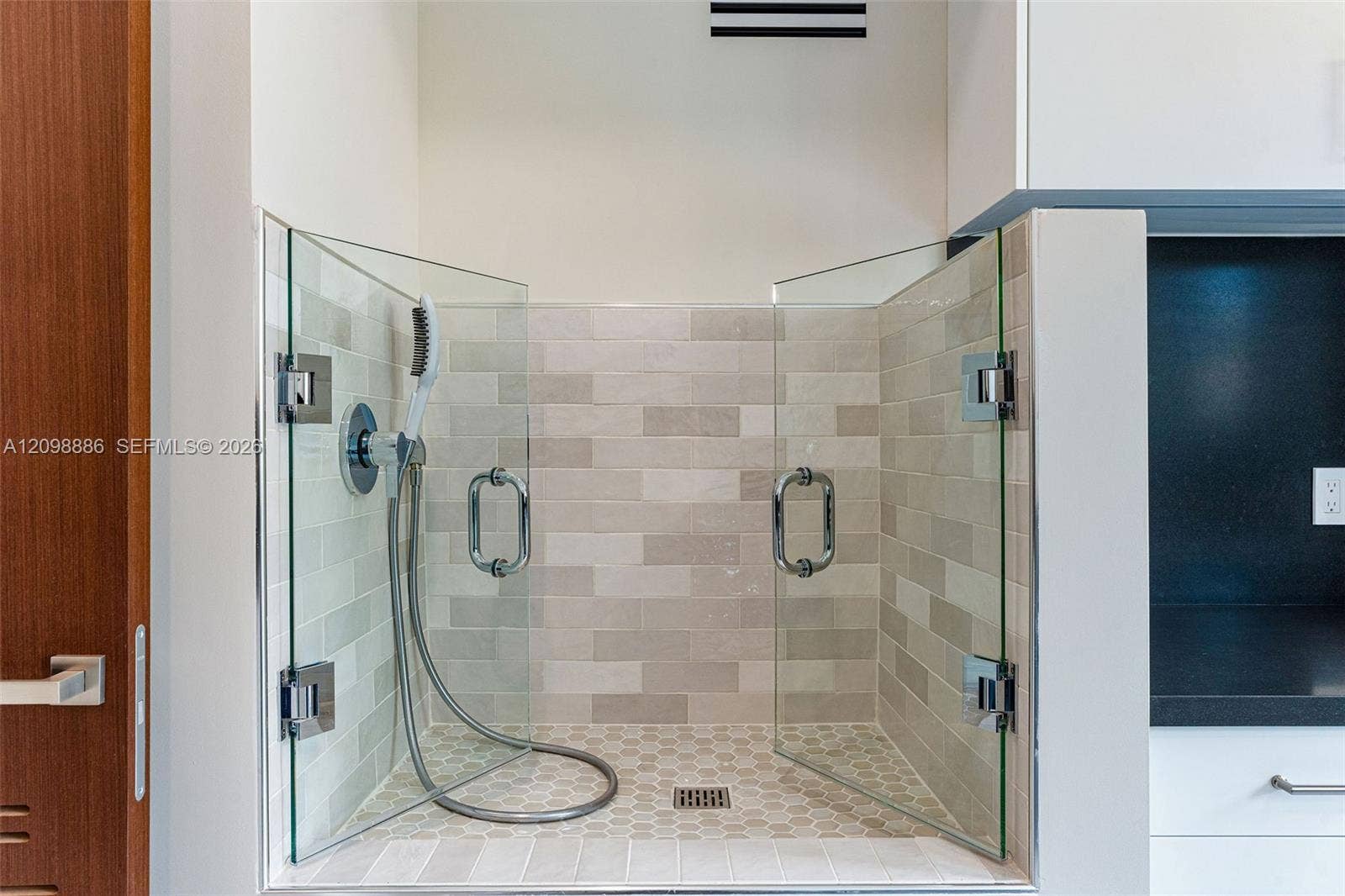 Glass-enclosed station featuring a handheld shower fixture, subway-tile wall surround, hexagonal floor tile, and polished chrome hardware