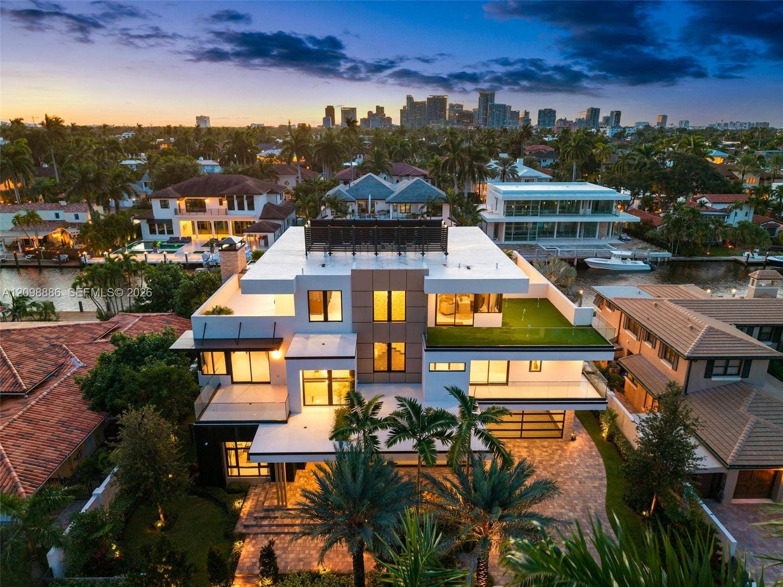 Multi-level contemporary residence featuring a rooftop terrace, tiered balconies with glass railings, composite stone exterior detailing, integrated rooftop solar panels, and paver-stone driveway