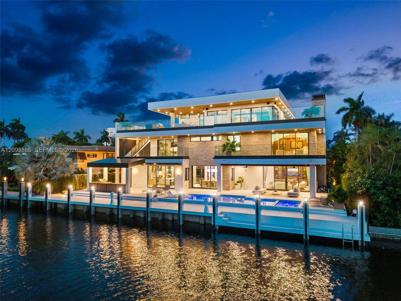 Multi-story modern residence featuring stone veneer siding, expansive glass sliders, multiple tiered balconies with glass railings, a swimming pool, and a private concrete dock