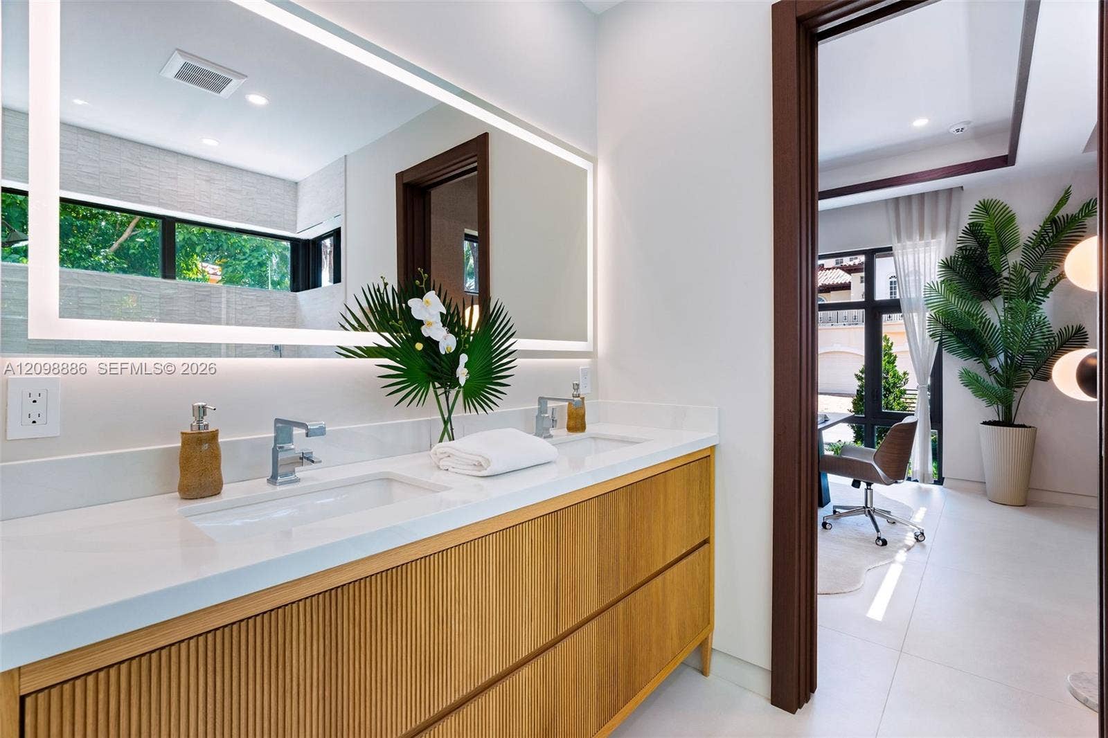 Floating dual-sink vanity with ribbed wood-finish cabinetry, solid-surface countertop, integrated LED-backlit mirror, and polished chrome faucets
