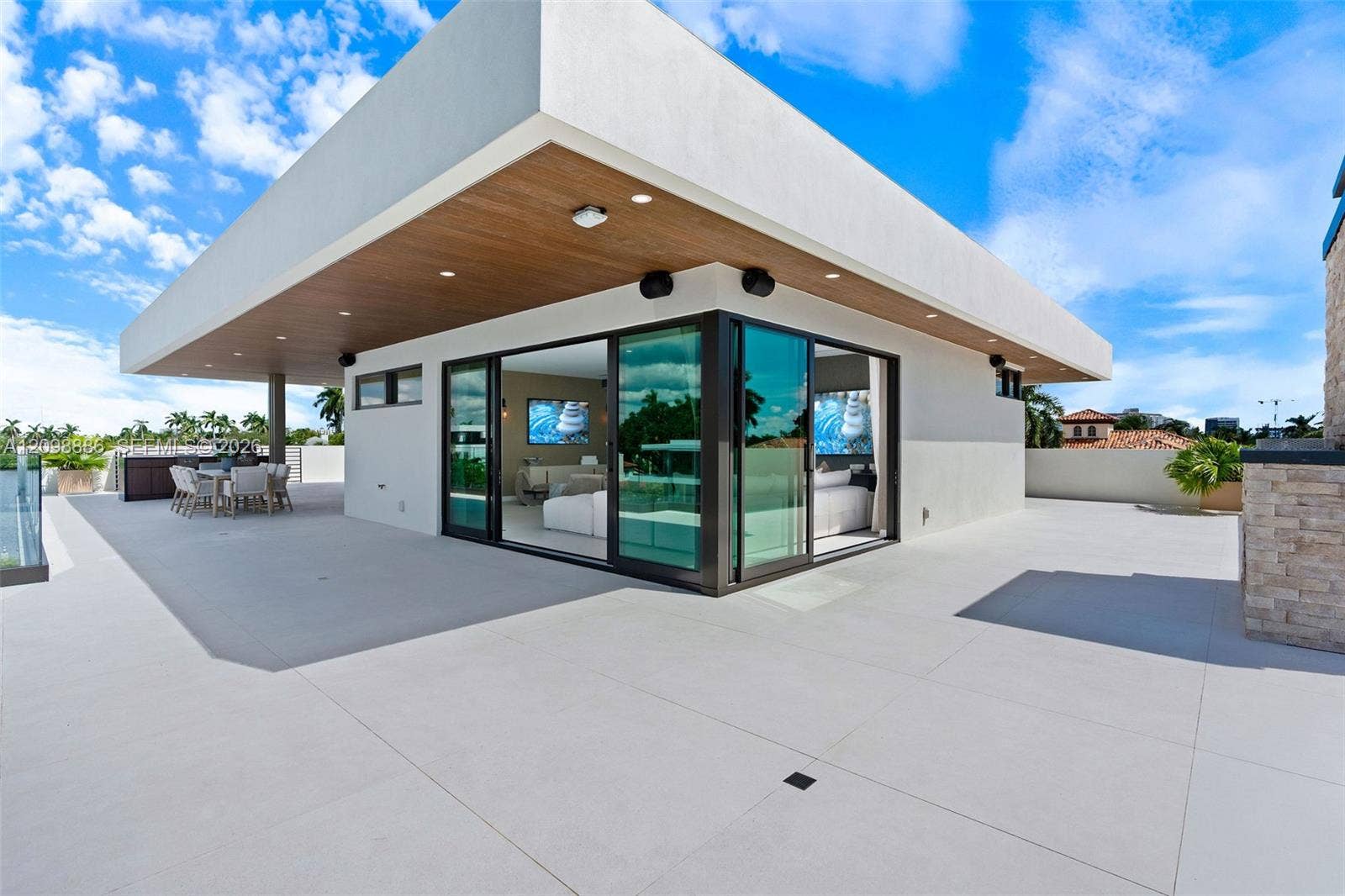 Expansive rooftop terrace featuring large-format tile flooring, a cantilevered roof overhang with wood-finish soffits, recessed lighting, and floor-to-ceiling multi-panel sliding glass doors