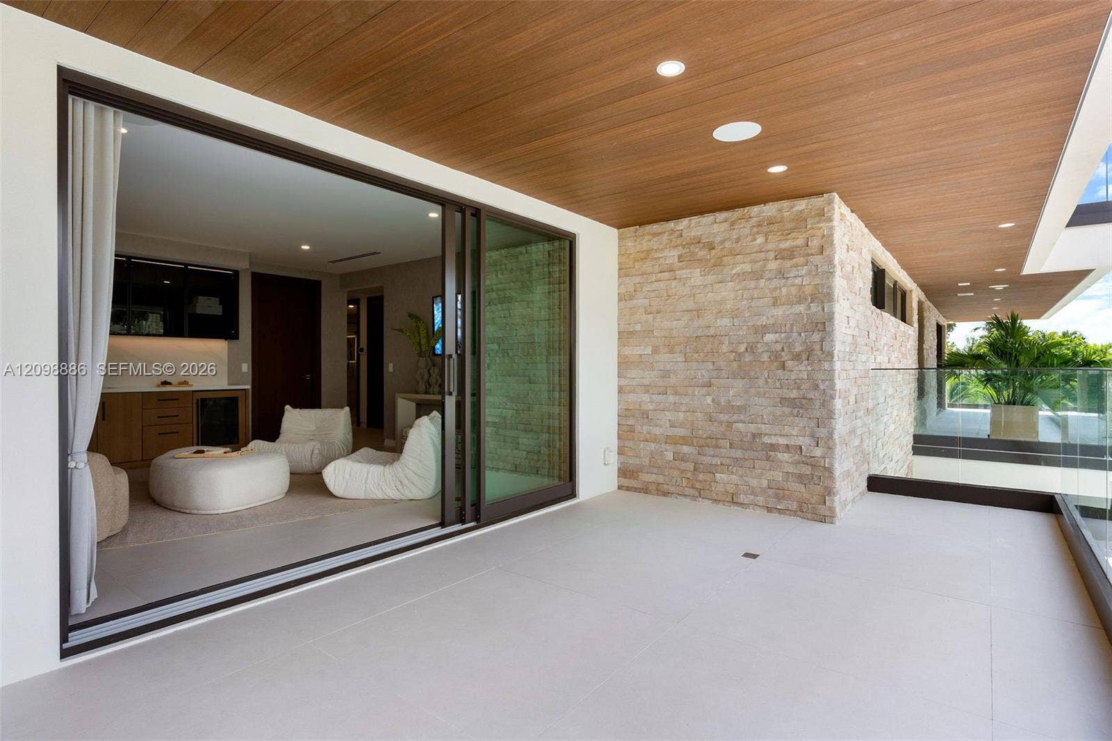Covered balcony featuring wood-plank ceiling, large-format tile flooring, stacked-stone accent wall, recessed lighting, and expansive glass sliding doors