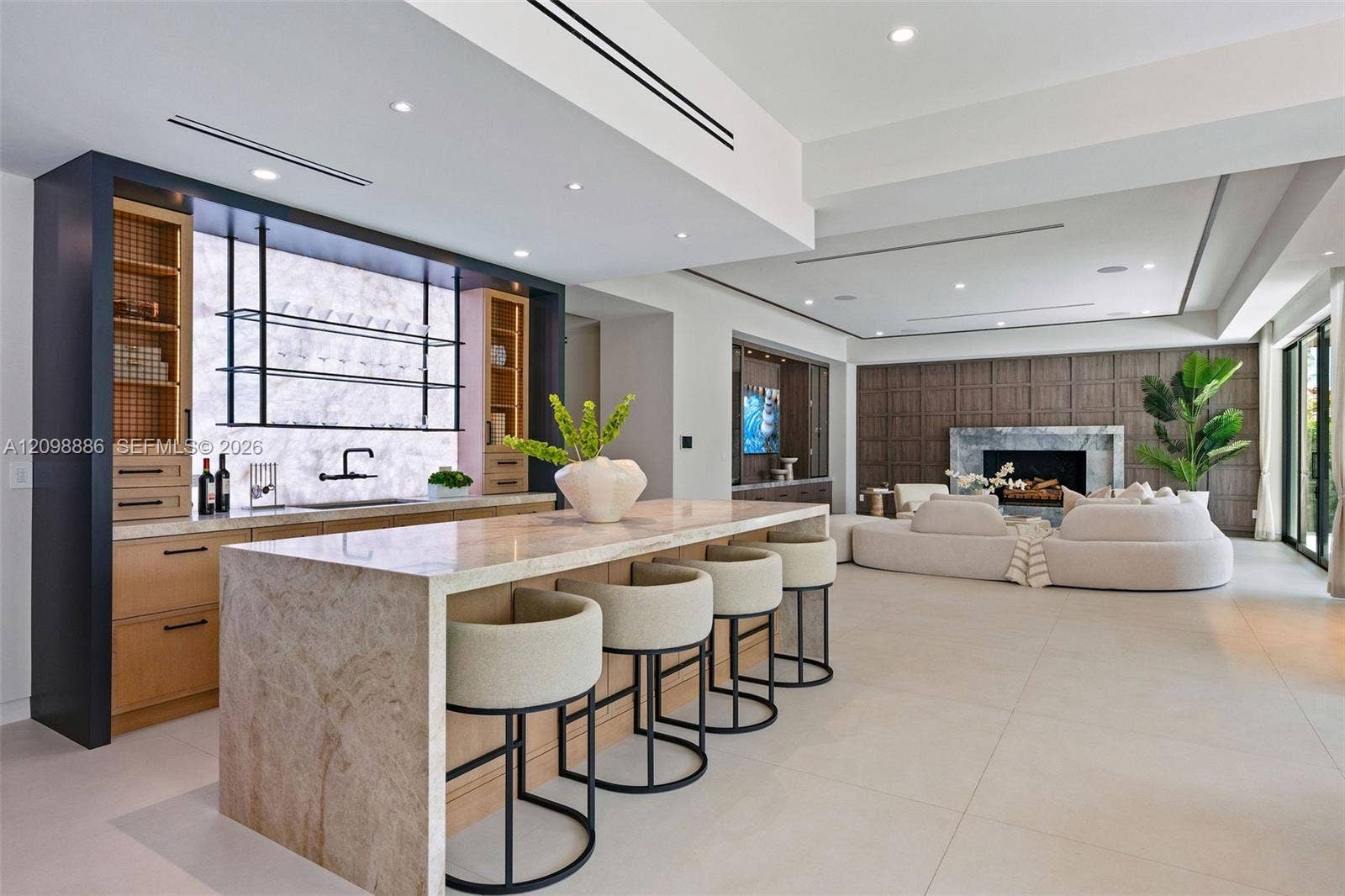 Stone-topped kitchen island with bar seating, custom cabinetry featuring integrated shelving, recessed lighting, and floor-to-ceiling wood wall paneling with an inset fireplace