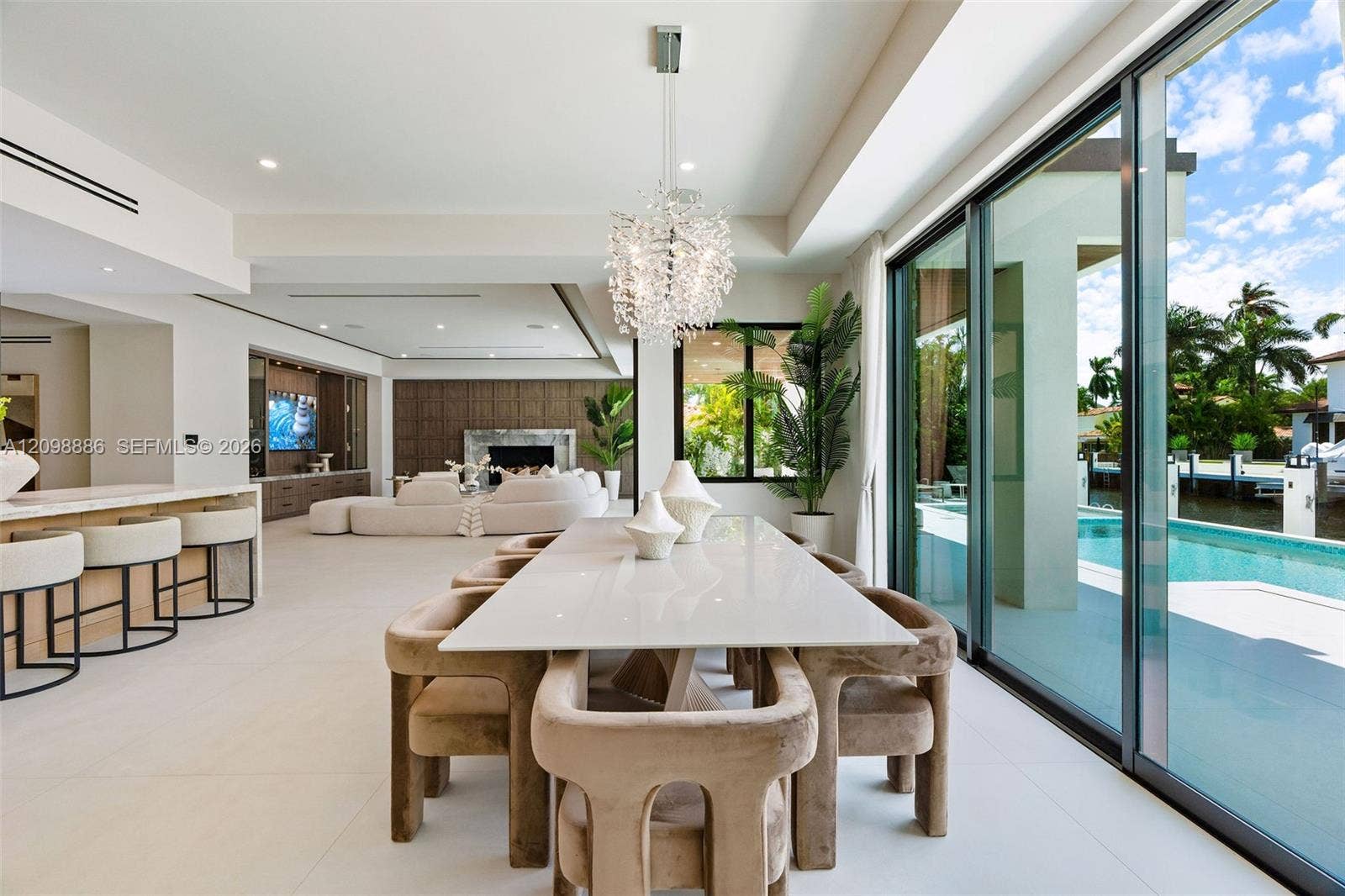 Open-concept interior featuring large-format tile flooring, a statement crystal chandelier, built-in cabinetry, a fireplace with stone surround, and floor-to-ceiling sliding glass doors opening to a pool and canal