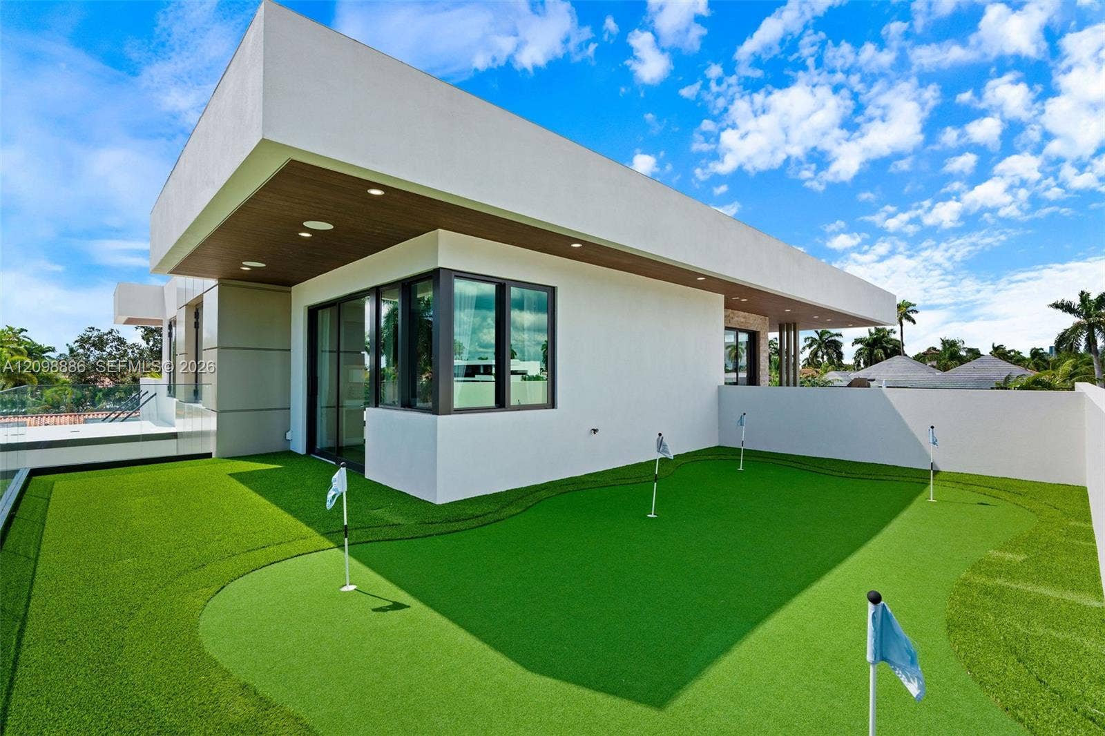 Contemporary rooftop terrace featuring a multi-hole putting green, synthetic turf surfacing, flat-roof architecture, recessed ceiling lighting, and floor-to-ceiling glass windows