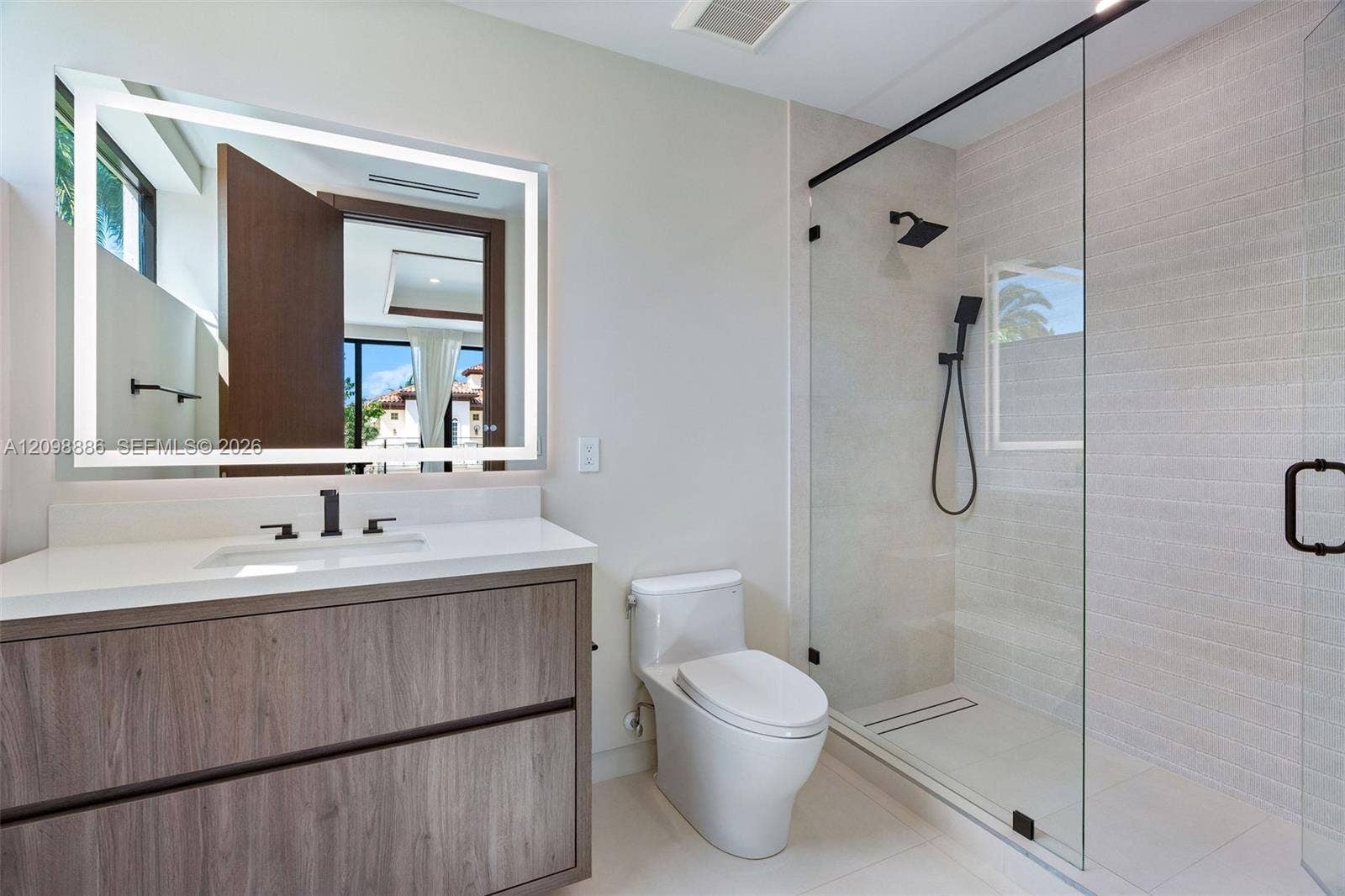 Wood-finish floating vanity with a quartz countertop, backlit LED mirror, and matte black plumbing fixtures