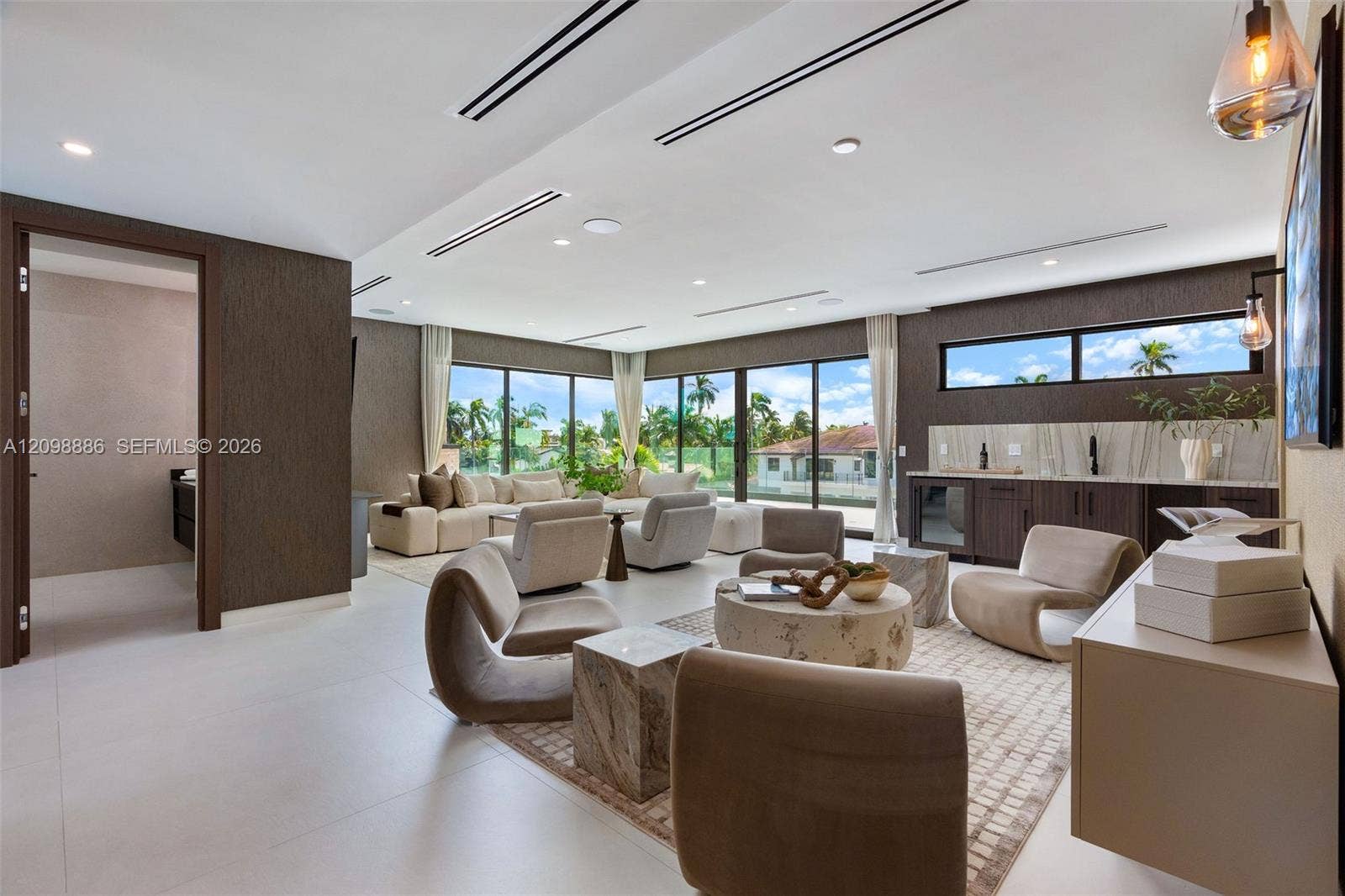 Large-format tile flooring, recessed linear lighting, floor-to-ceiling glass sliding doors, built-in wet bar with stone backsplash, and dark textured wall treatments