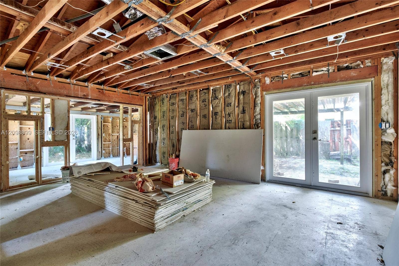 1176 SW 4th Street, Boca Raton, FL 33486 Open-concept interior featuring exposed wooden rafters, dual sets of double glass doors, and concrete slab flooring