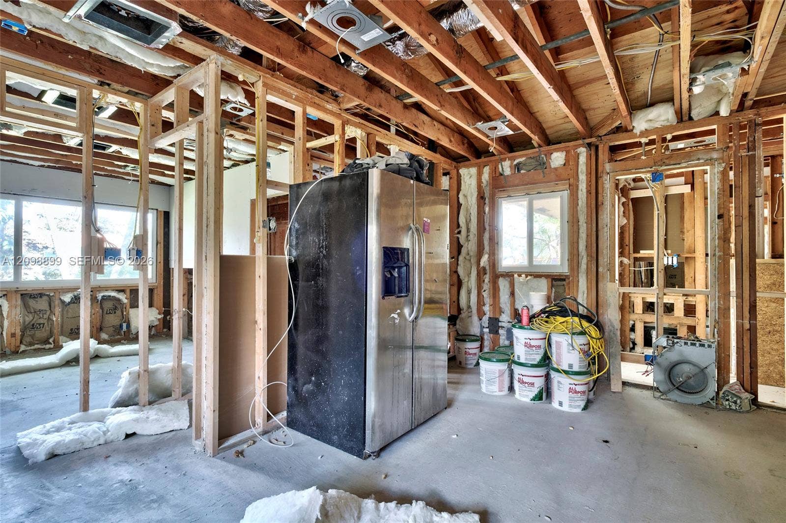 1176 SW 4th Street, Boca Raton, FL 33486 Interior space featuring exposed wood framing, concrete flooring, stainless steel side-by-side refrigerator, multi-pane windows, and thermal insulation