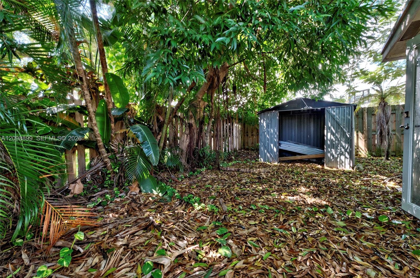 1176 SW 4th Street, Boca Raton, FL 33486 Outdoor space featuring a metal storage shed, wood fencing, and mature tropical trees