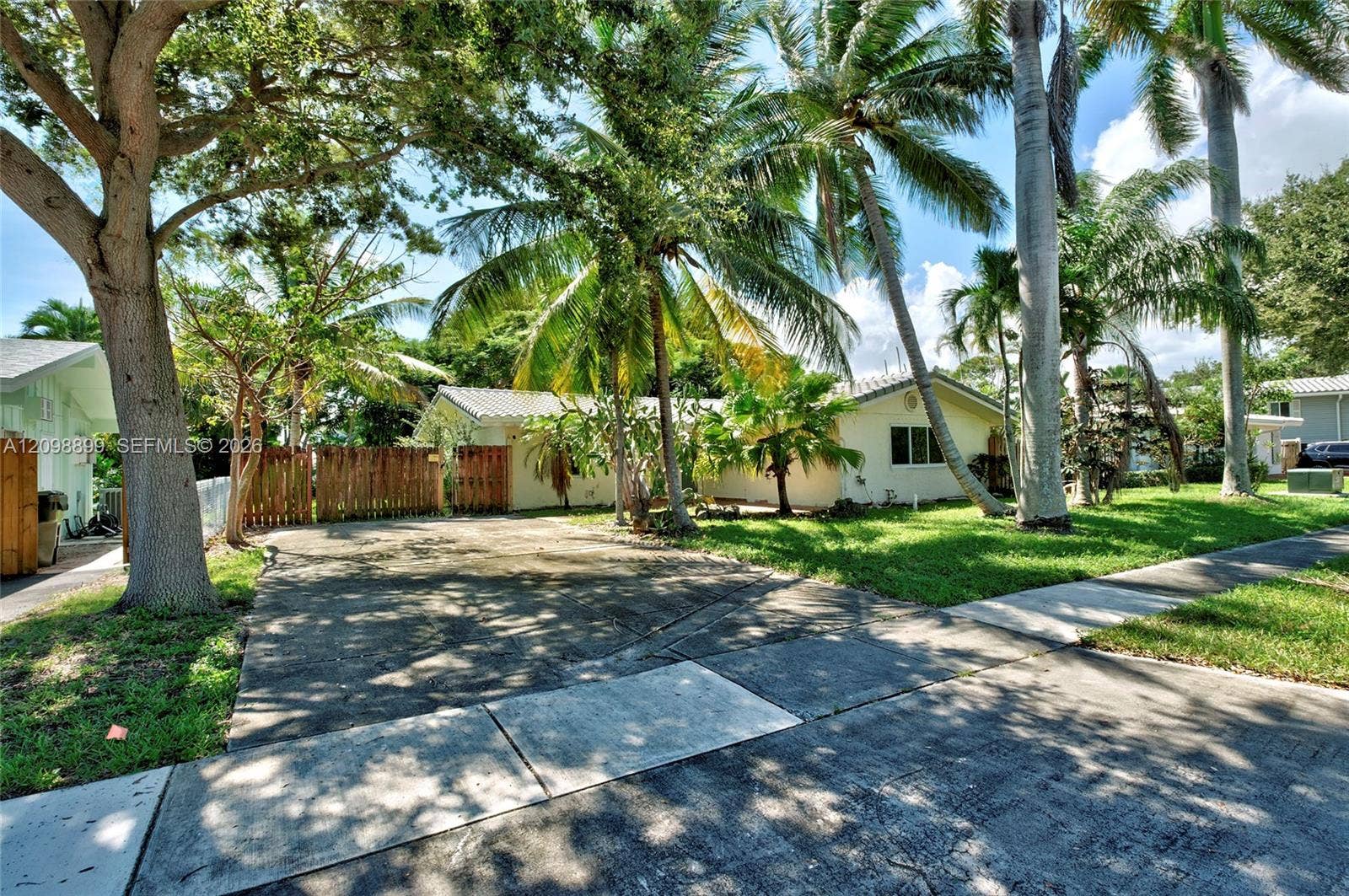 1176 SW 4th Street, Boca Raton, FL 33486 Single-story residence featuring a concrete driveway, wooden privacy fencing, tiled roofing, and mature palm trees