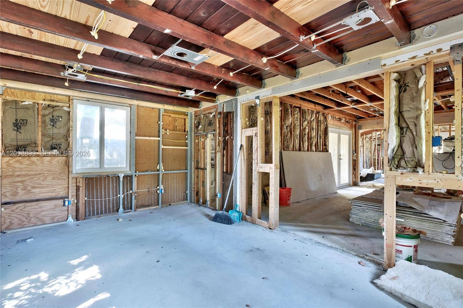 1176 SW 4th Street, Boca Raton, FL 33486 Interior space featuring exposed wood-beam ceiling, concrete flooring, and an exterior window with glass panes