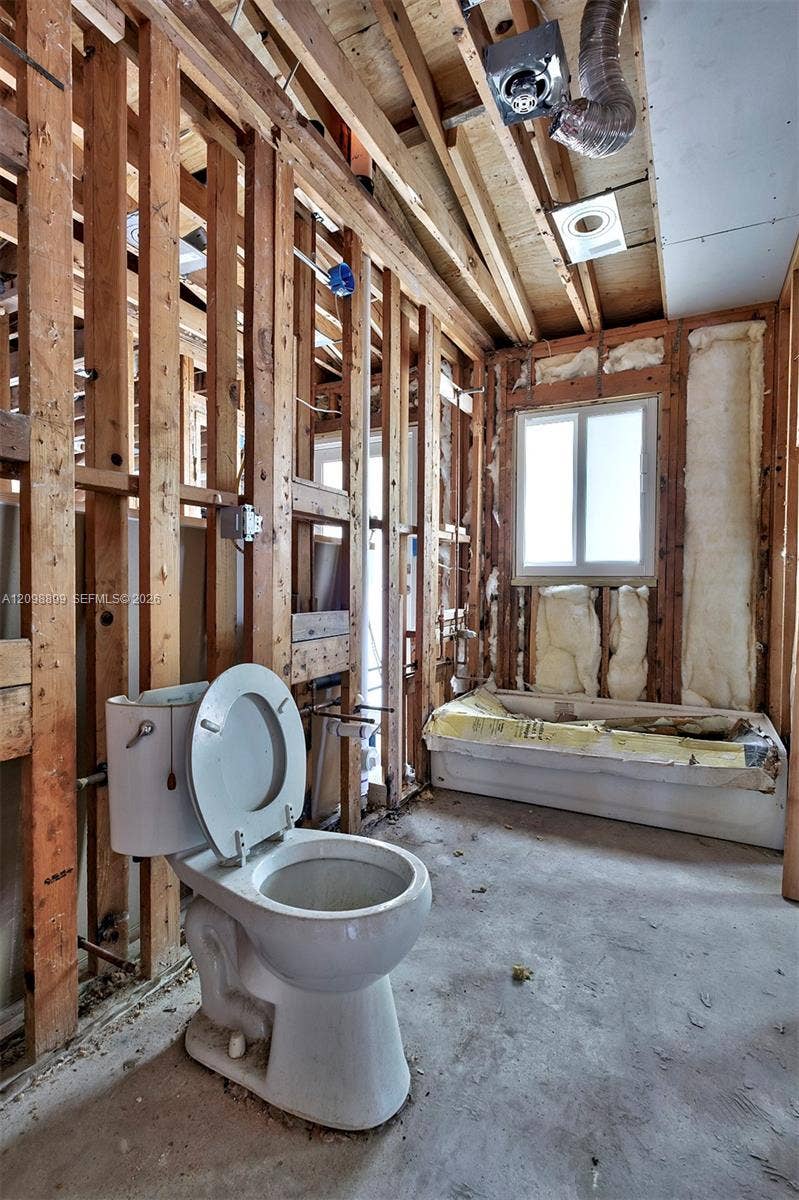 1176 SW 4th Street, Boca Raton, FL 33486 Interior space featuring exposed wood framing, concrete flooring, a white bathtub, a single-flush toilet, and a window
