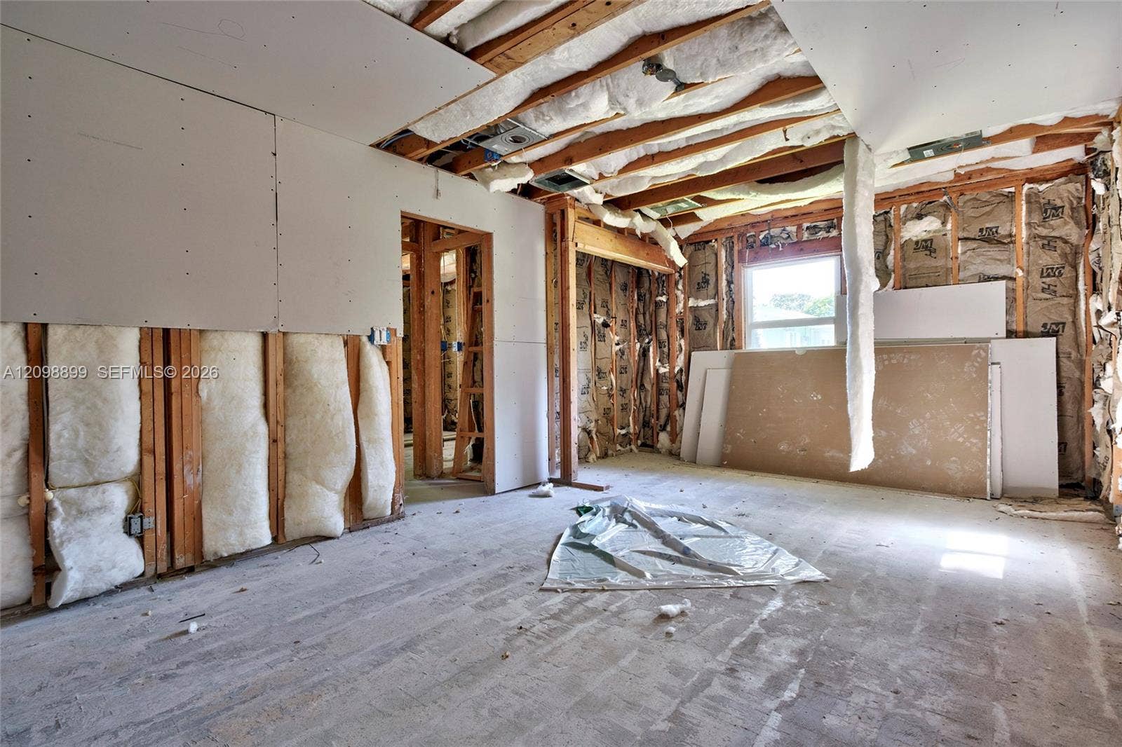 1176 SW 4th Street, Boca Raton, FL 33486 Interior space featuring exposed wood framing, installed batt insulation, partially applied drywall panels, and a single window