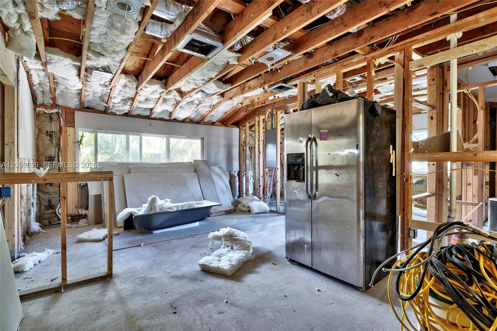 1176 SW 4th Street, Boca Raton, FL 33486 Open-concept interior space featuring exposed wooden ceiling joists, wall studs, stainless steel double-door refrigerator, and large window