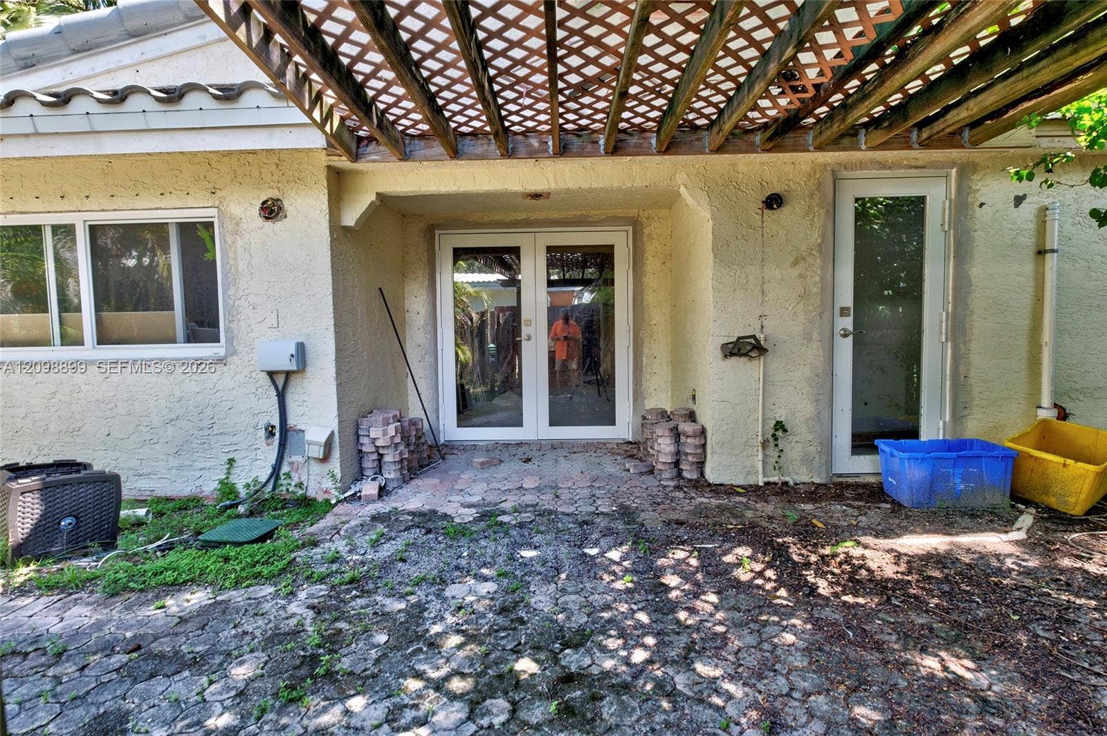 1176 SW 4th Street, Boca Raton, FL 33486 Exterior patio space featuring a latticed wood-frame pergola, stone paver flooring, double-glass entry doors, and a secondary single-glass door