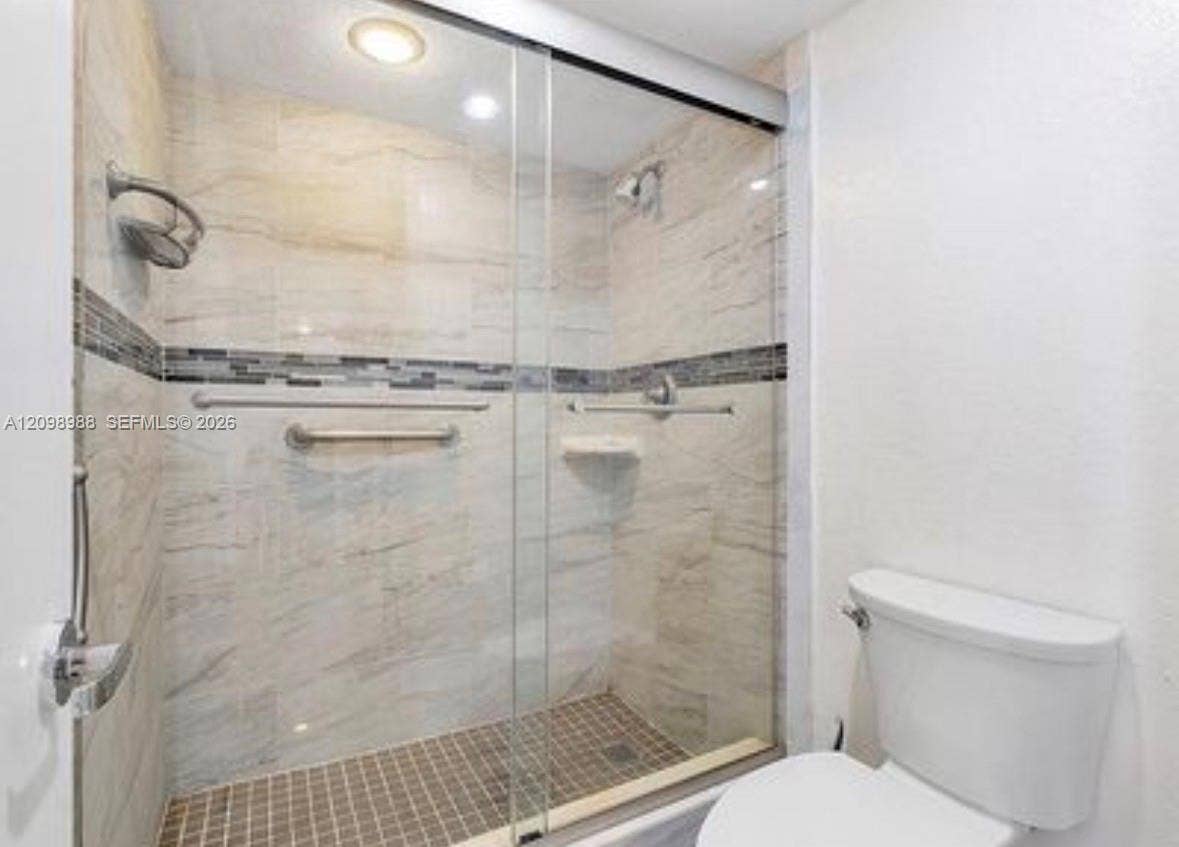 Spa-inspired ensuite bathroom featuring a frameless glass-enclosed shower with dual showerheads, linear tile accent band, tile flooring, and polished chrome fixtures throughout