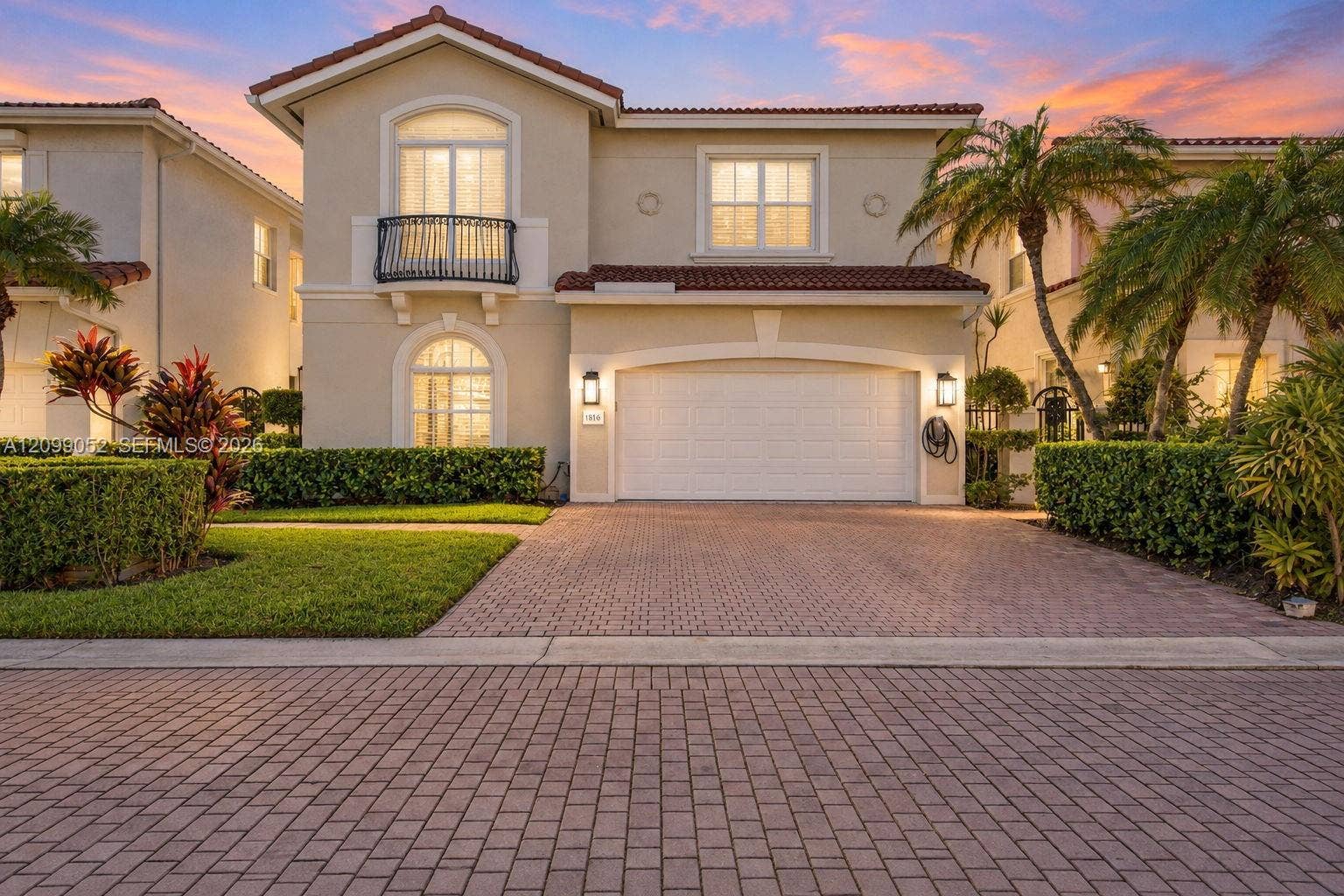 1516 Breakwater Terrace, Hollywood, FL 33019 Stucco exterior featuring a terracotta tile roof, second-story balcony with metal railing, arched window detailing, and brick-paver driveway