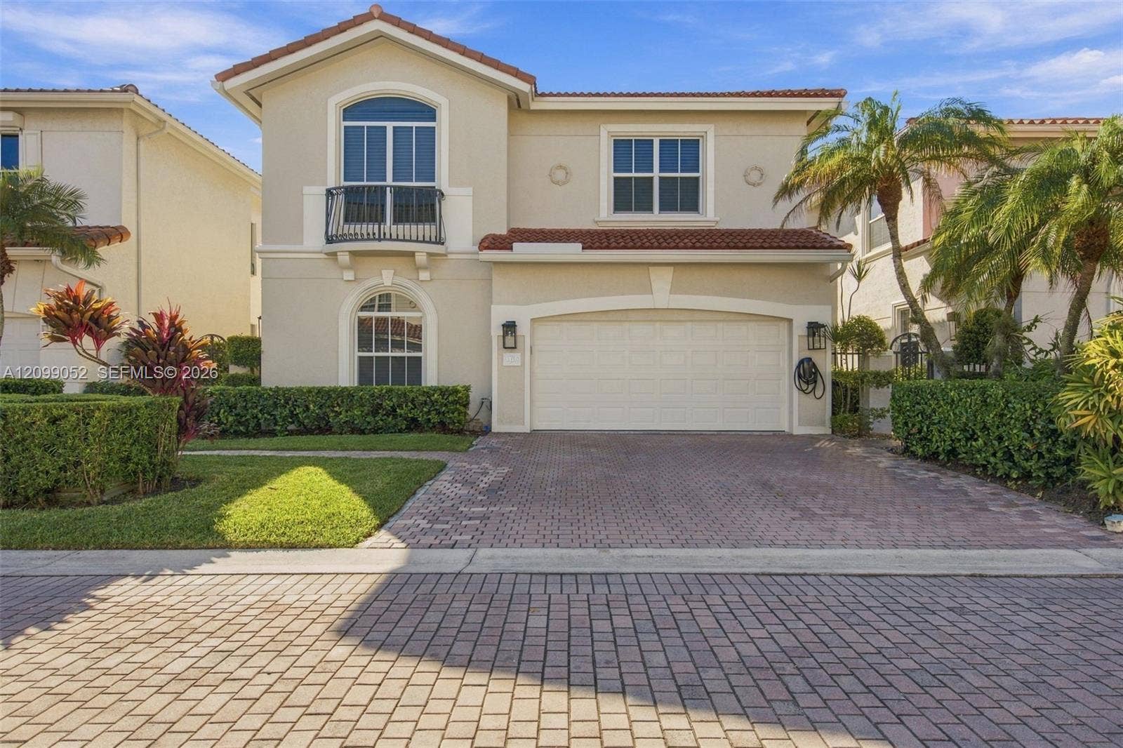 1516 Breakwater Terrace, Hollywood, FL 33019 Two-story stucco exterior featuring a tile roof, an arched balcony with metal railing, and a paver driveway leading to a two-car garage