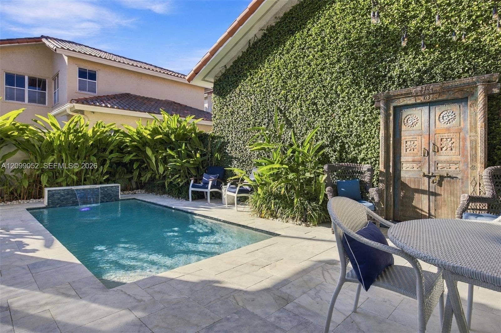 1516 Breakwater Terrace, Hollywood, FL 33019 Outdoor space featuring a swimming pool with a built-in water feature, stone paver decking, decorative wood-carved gate, and exterior wall with climbing vegetation