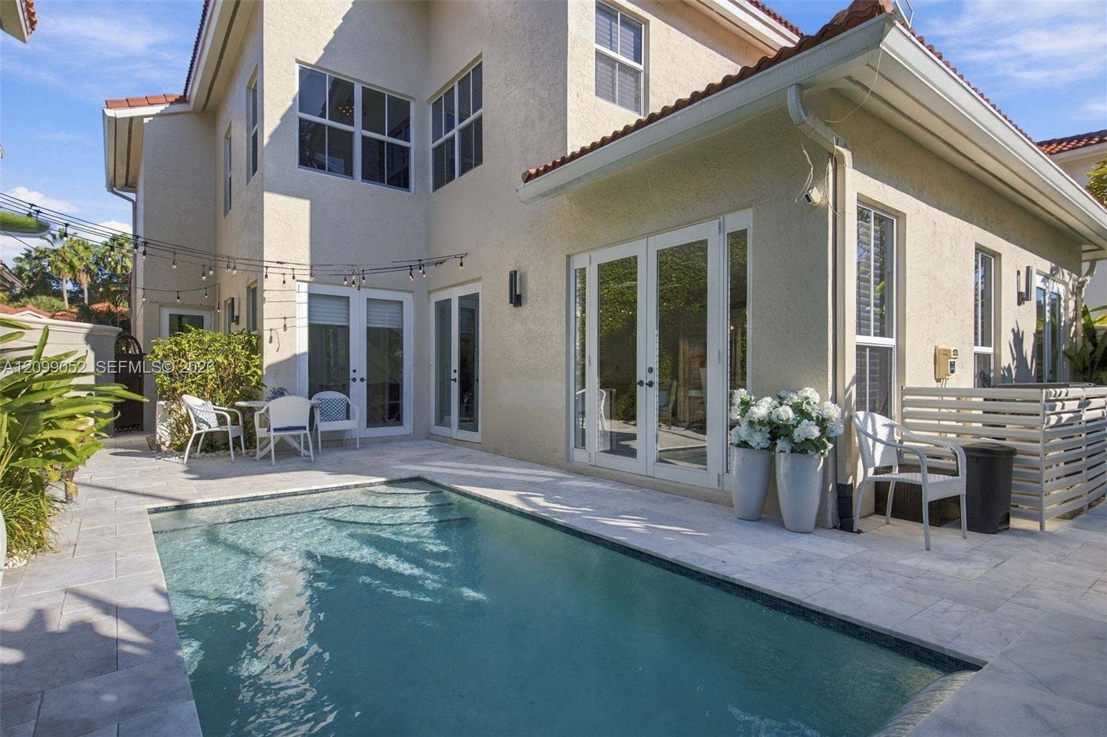 1516 Breakwater Terrace, Hollywood, FL 33019 Stucco exterior featuring a rectangular inground pool, stone-paver decking, multiple sets of glass double doors, and a tile roof