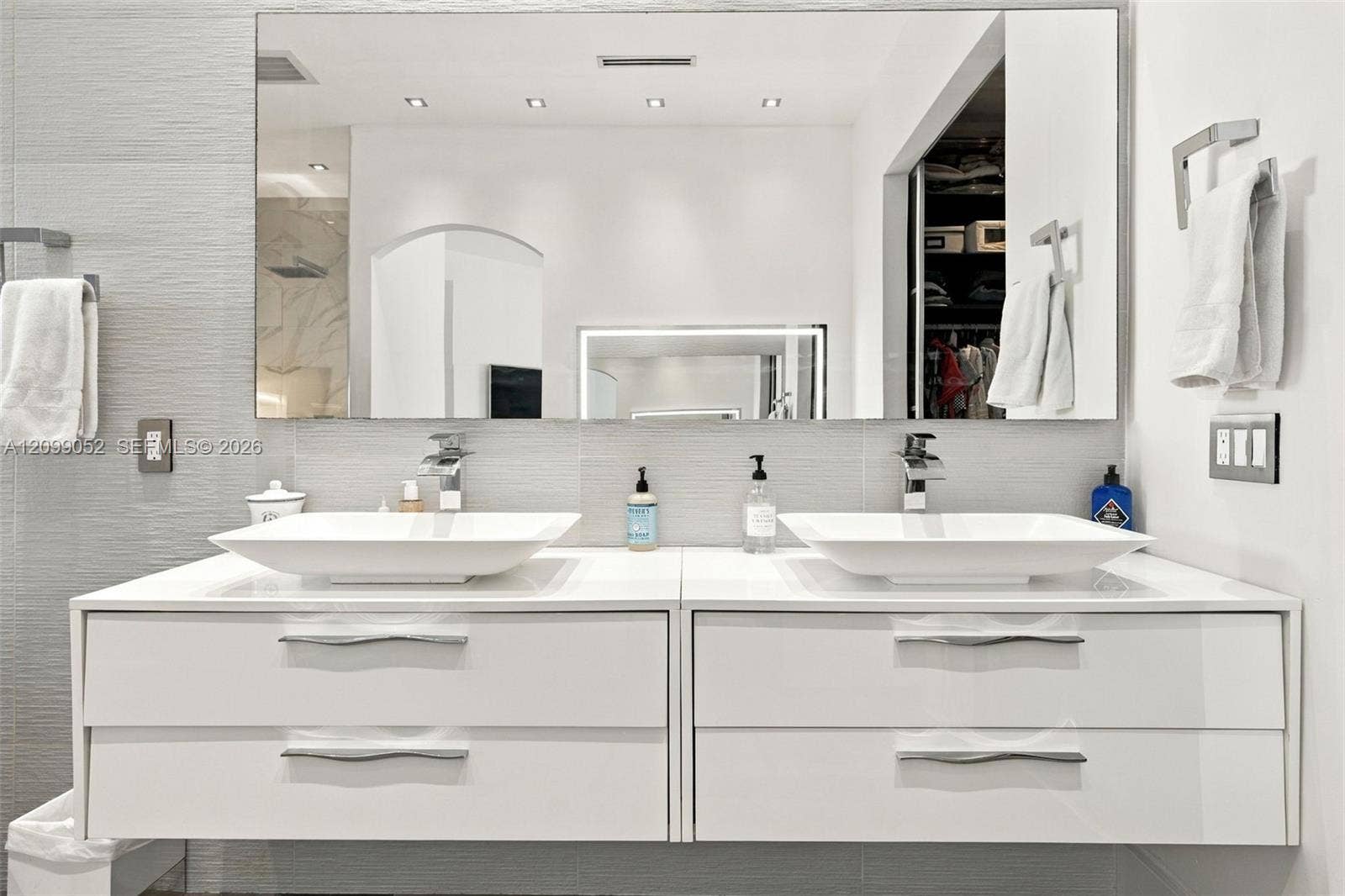 1516 Breakwater Terrace, Hollywood, FL 33019 Floating dual vanity featuring white cabinetry, rectangular vessel sinks, chrome faucets, and large wall-mounted mirror with recessed lighting