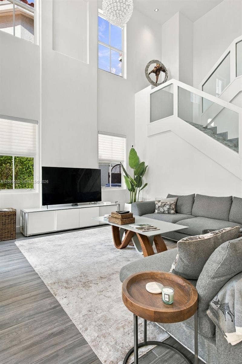 1516 Breakwater Terrace, Hollywood, FL 33019 High-ceiling interior featuring multiple oversized windows, wood-finish flooring, glass-panel stair railing, and a tiered spherical chandelier