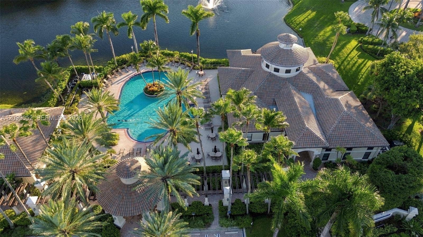 1516 Breakwater Terrace, Hollywood, FL 33019 Aerial perspective featuring a clubhouse with a tiled hip roof, a paved pool deck, a swimming pool with a central island, a detached gazebo, and extensive landscaping