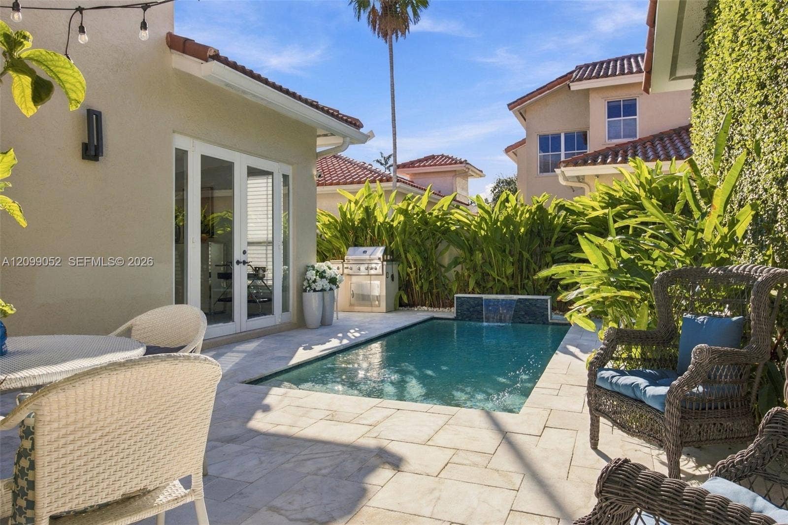 1516 Breakwater Terrace, Hollywood, FL 33019 Outdoor living space featuring a tiled patio, private swimming pool with a stone-accented water feature, built-in stainless steel grill, and manicured perimeter landscaping