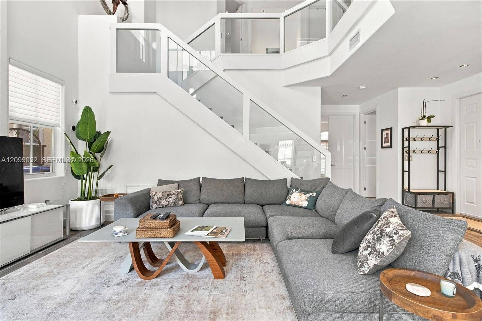 1516 Breakwater Terrace, Hollywood, FL 33019 Double-height living area featuring a custom glass and white-frame staircase railing, recessed lighting, and large windows with horizontal blinds