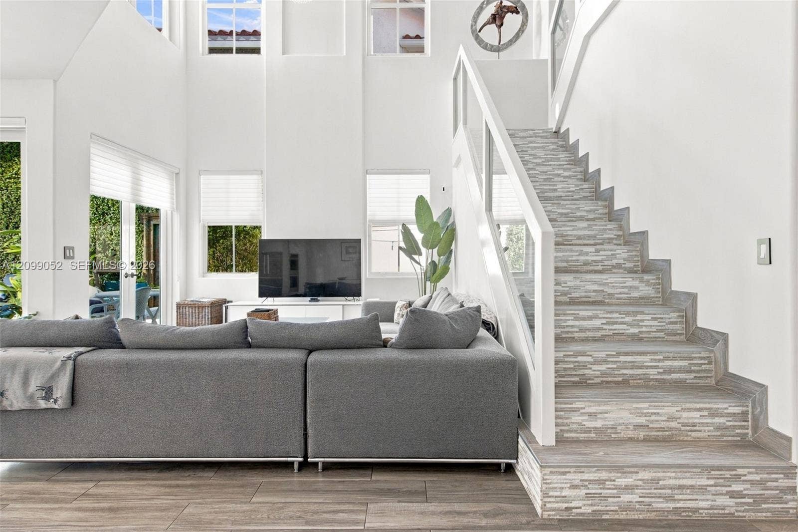 1516 Breakwater Terrace, Hollywood, FL 33019 Double-height ceiling, open floor plan featuring wood-finish flooring, staircase with tiled risers, white railing, and glass paneled walls, and multiple large windows with cellular shades
