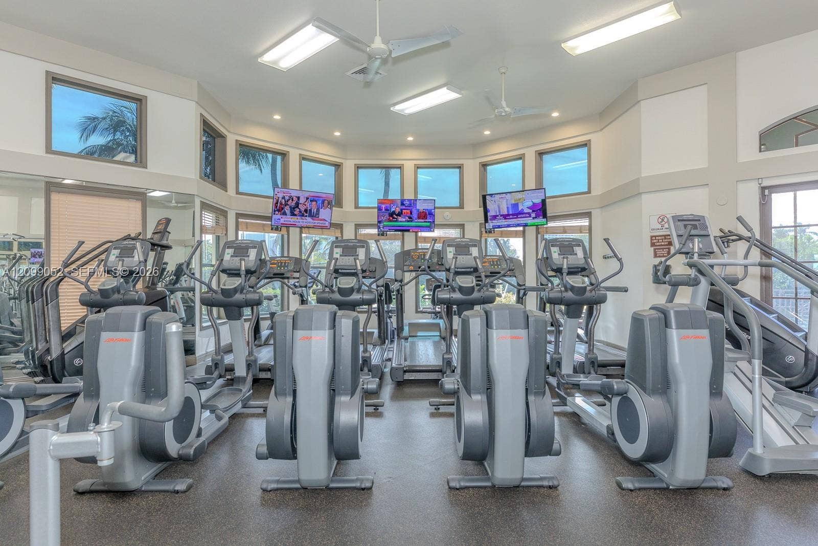 1516 Breakwater Terrace, Hollywood, FL 33019 Fitness center featuring a high-vaulted ceiling, multiple rows of windows, rubberized flooring, and dual ceiling fans