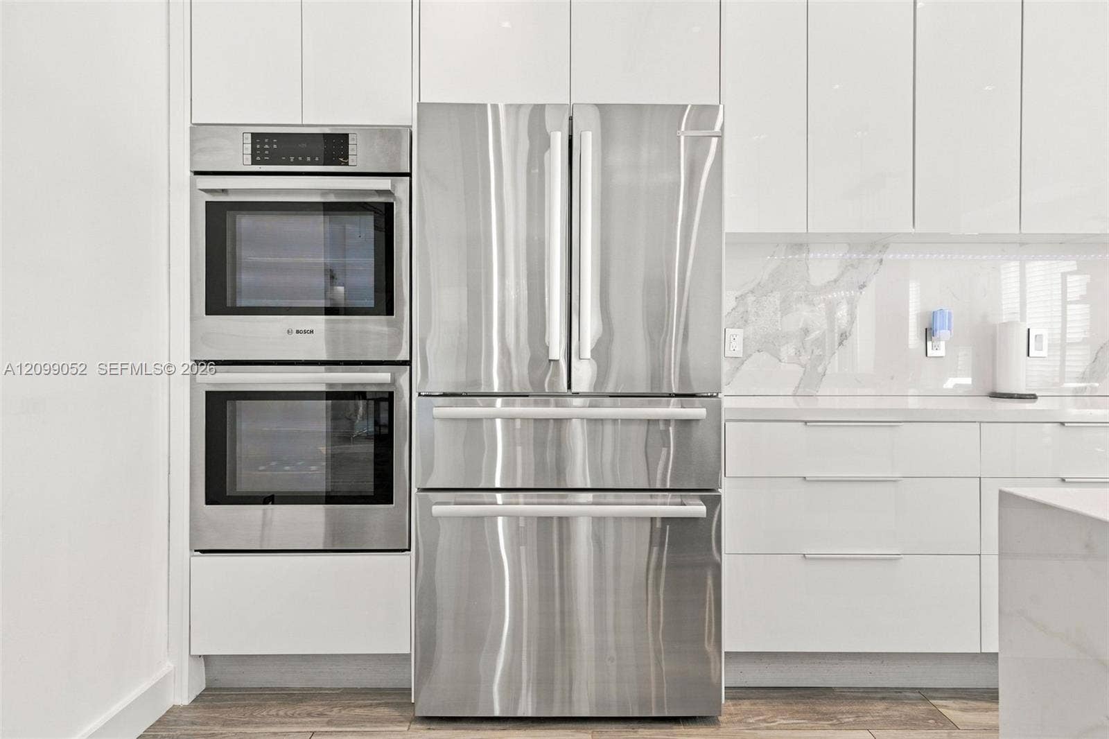 1516 Breakwater Terrace, Hollywood, FL 33019 Kitchen featuring high-gloss white cabinetry, stainless steel double wall ovens, a stainless steel French-door refrigerator, stone-composite backsplash, and wood-finish flooring