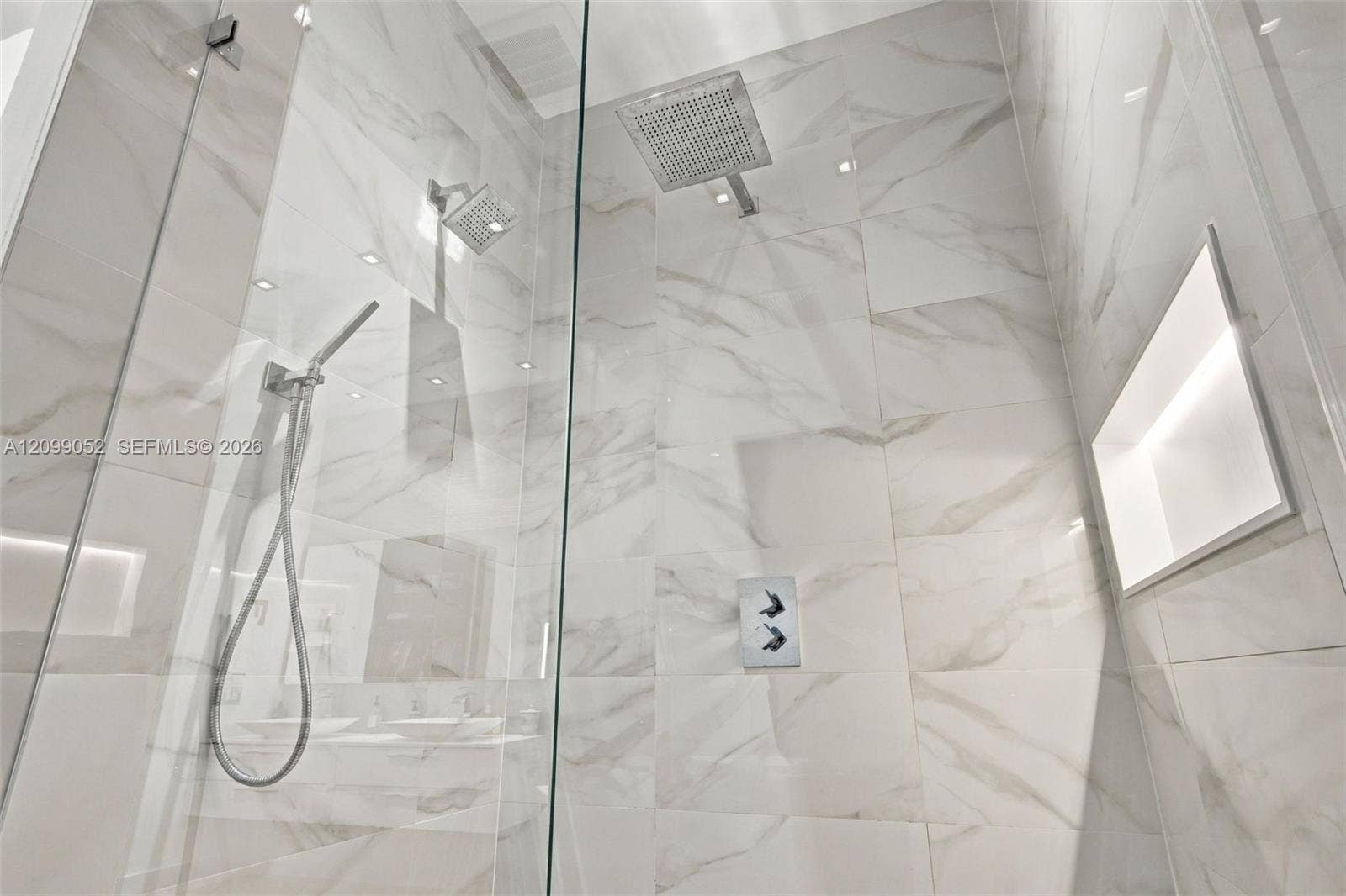 1516 Breakwater Terrace, Hollywood, FL 33019 Walk-in shower featuring large-format light veined tile, frameless glass enclosure, ceiling-mounted rainfall showerhead, adjustable handheld shower wand, and integrated recessed shelving with integrated lighting