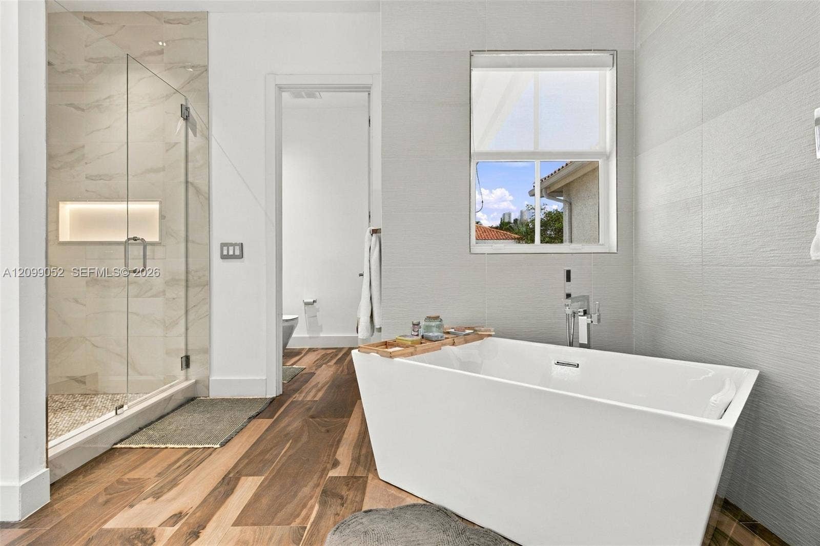 1516 Breakwater Terrace, Hollywood, FL 33019 Freestanding soaking tub with chrome wall-mounted faucet, glass-enclosed shower with tiled walls and built-in recessed niche, and wood-finish flooring