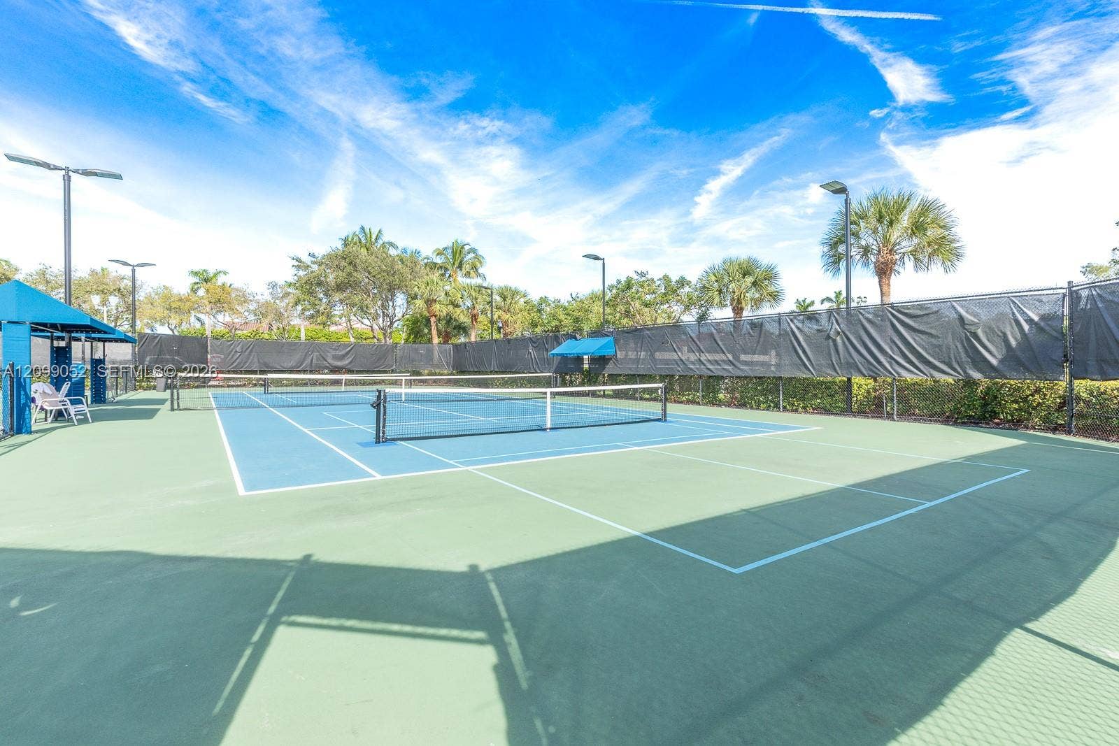 1516 Breakwater Terrace, Hollywood, FL 33019 Tennis court featuring a multi-tone hard surface, perimeter fencing, overhead lighting, and shaded seating areas