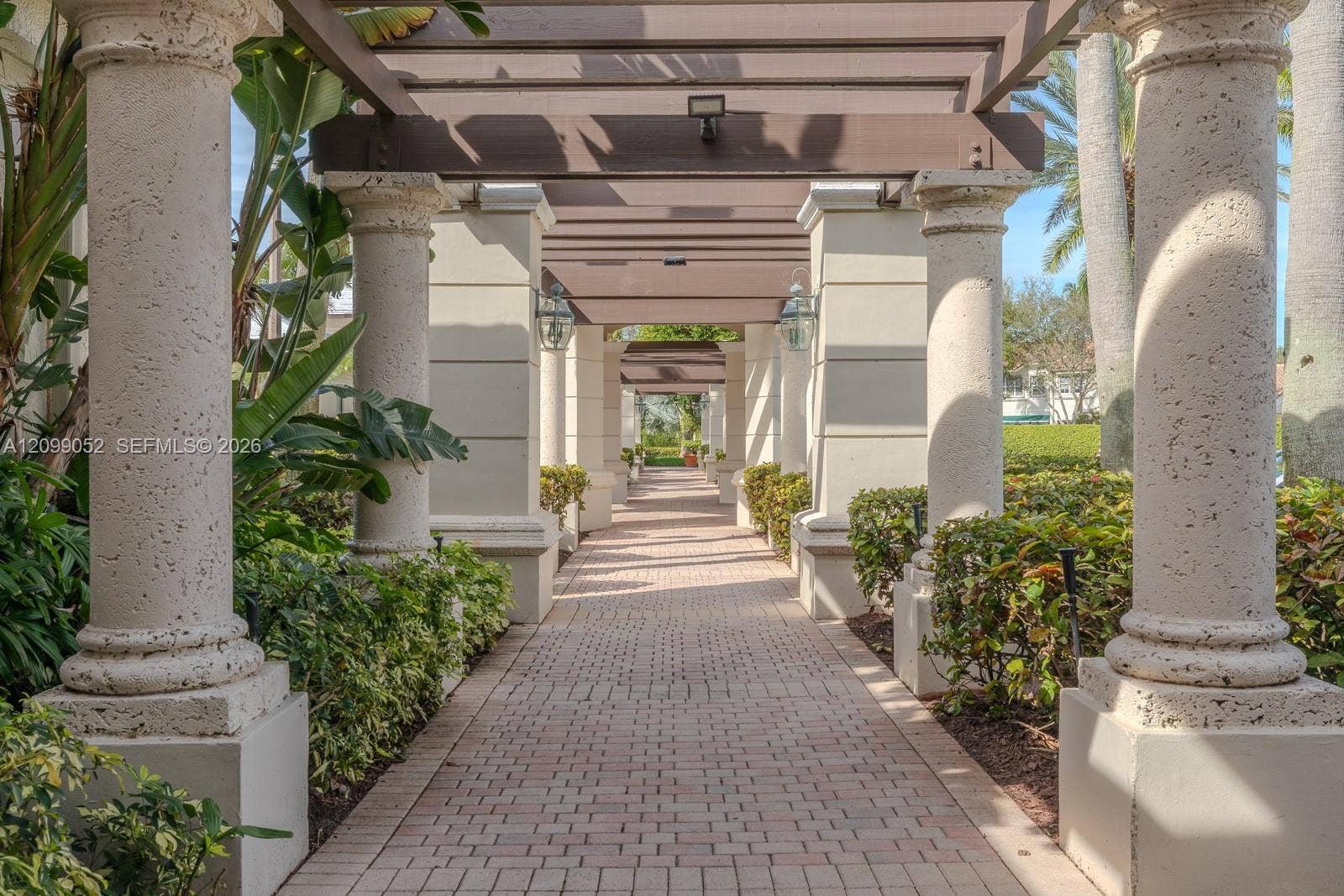 1516 Breakwater Terrace, Hollywood, FL 33019 Outdoor walkway featuring a brick-paver path, structural stone columns, overhead timber-frame pergola, and integrated wall-mounted lantern lighting