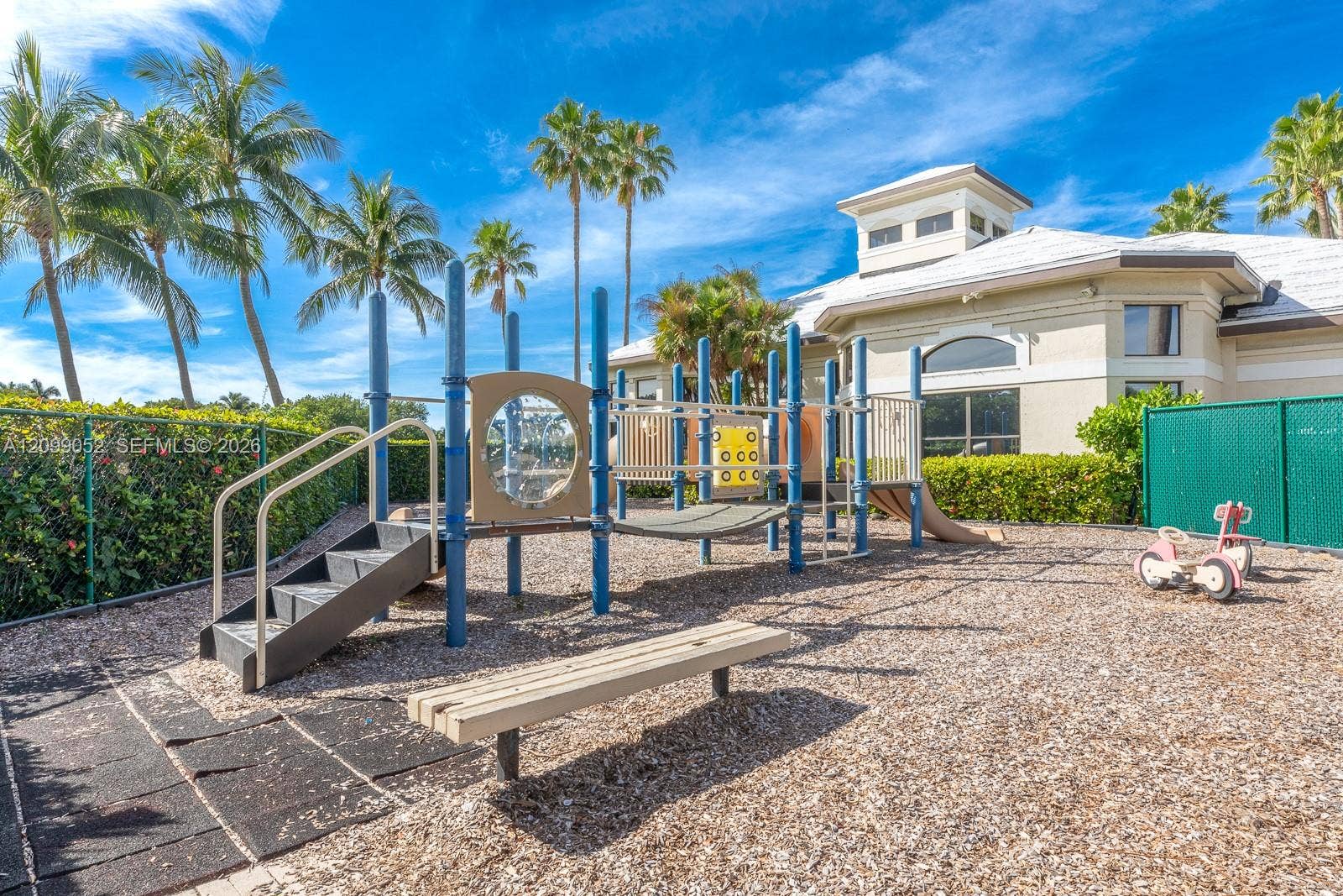 1516 Breakwater Terrace, Hollywood, FL 33019 Recreational area featuring a multi-component play structure, wood-chip surface, built-in bench seating, and landscaped perimeter hedges