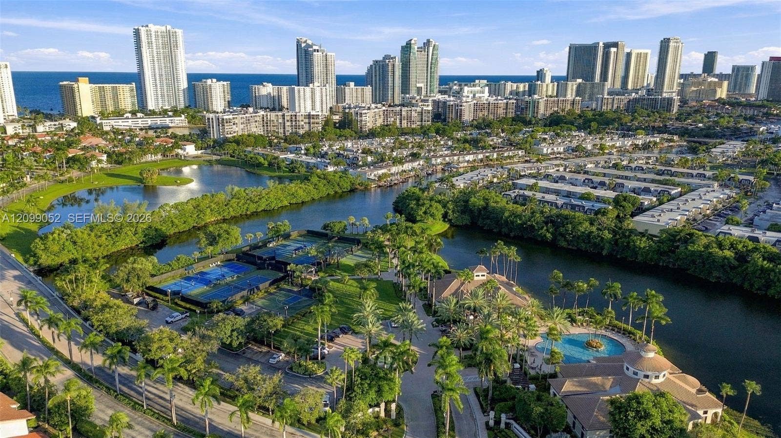 1516 Breakwater Terrace, Hollywood, FL 33019 Aerial perspective of the community featuring a swimming pool, multiple tennis courts, a central lagoon, and landscaped grounds with mature palm trees