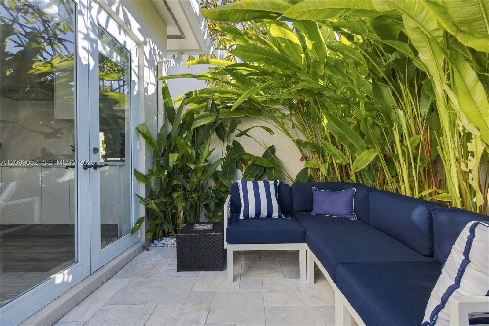 1516 Breakwater Terrace, Hollywood, FL 33019 Outdoor patio featuring natural stone pavers, double-glass swing doors, and perimeter privacy wall with lush tropical greenery