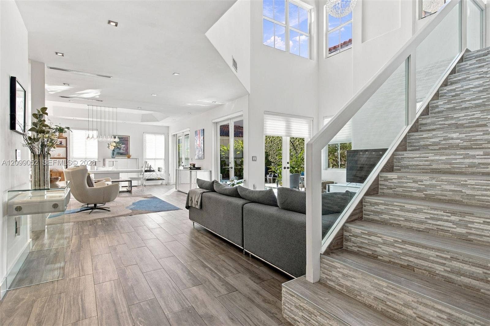 1516 Breakwater Terrace, Hollywood, FL 33019 Double-height ceiling, glass-paneled staircase railing, stacked stone-texture stair risers, wood-finish flooring, and multiple sets of French doors