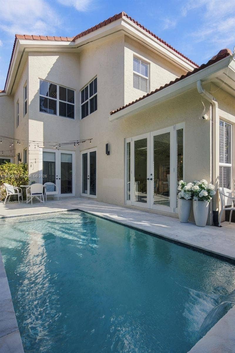 1516 Breakwater Terrace, Hollywood, FL 33019 Stucco exterior with a tiled roof, featuring multiple sets of white-framed glass paneled doors and a private swimming pool with stone paver decking