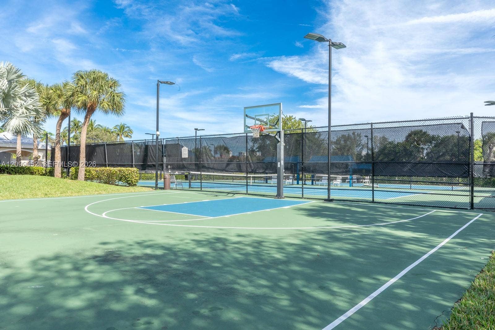 1516 Breakwater Terrace, Hollywood, FL 33019 Multi-sport hardcourt featuring a basketball hoop, perimeter chain-link fencing with privacy screens, and integrated high-mast lighting