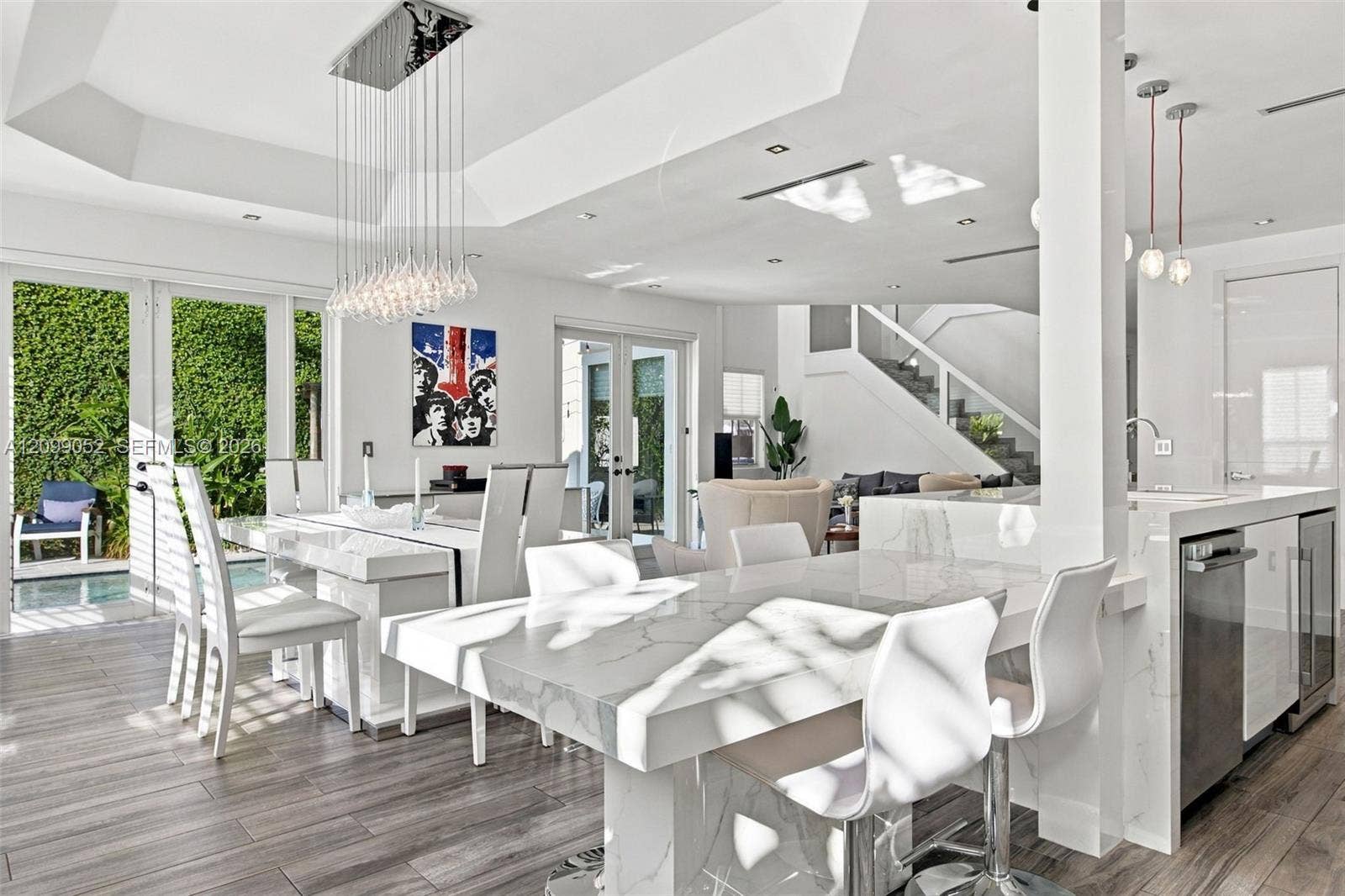 1516 Breakwater Terrace, Hollywood, FL 33019 Open-concept interior featuring a coffered ceiling, stone-surfaced waterfall island, wood-finish flooring, glass pendant lighting, and multi-panel glass doors