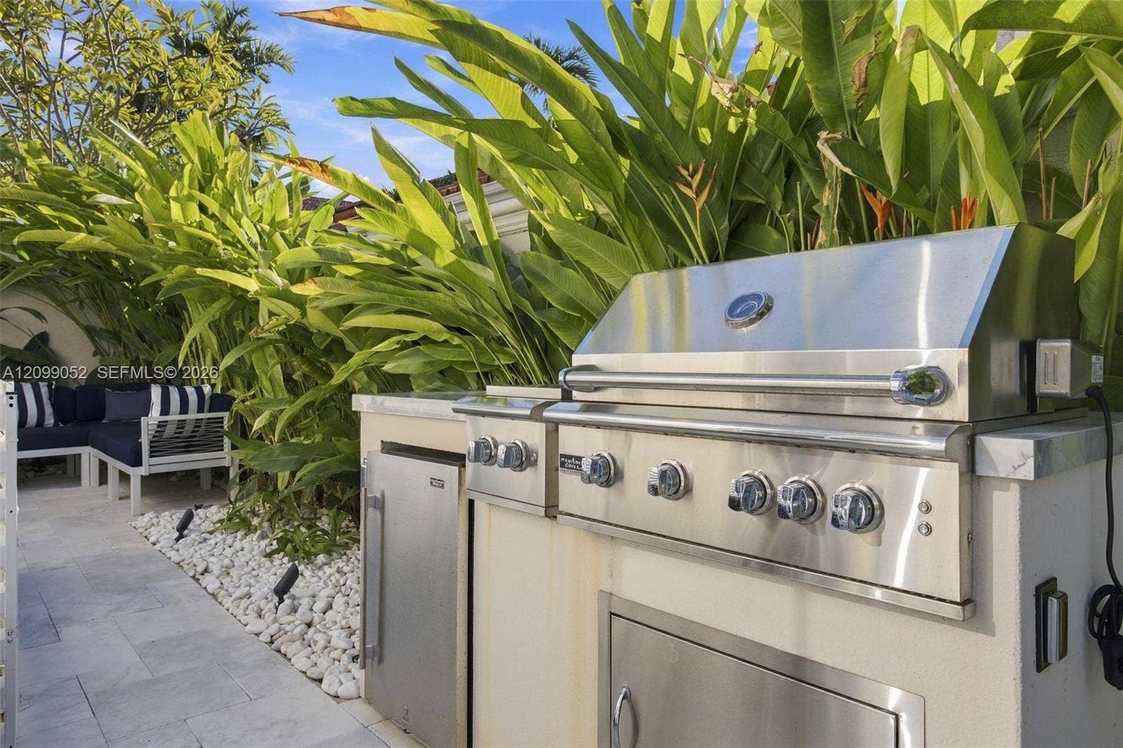 1516 Breakwater Terrace, Hollywood, FL 33019 Outdoor kitchen featuring a stainless steel grill, stone-surfaced countertops, custom built-in cabinetry, and integrated storage, set against a landscaped garden bed