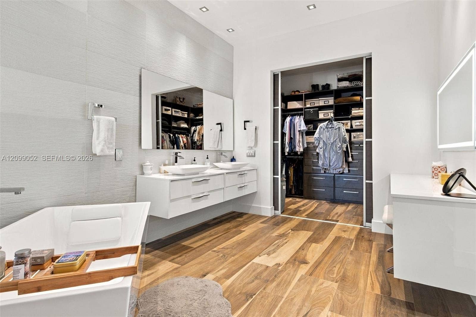 1516 Breakwater Terrace, Hollywood, FL 33019 Floating white dual-sink vanity with rectangular vessel sinks, freestanding deep-soaking tub, wood-finish flooring, and built-in closet system with sliding glass-panel doors