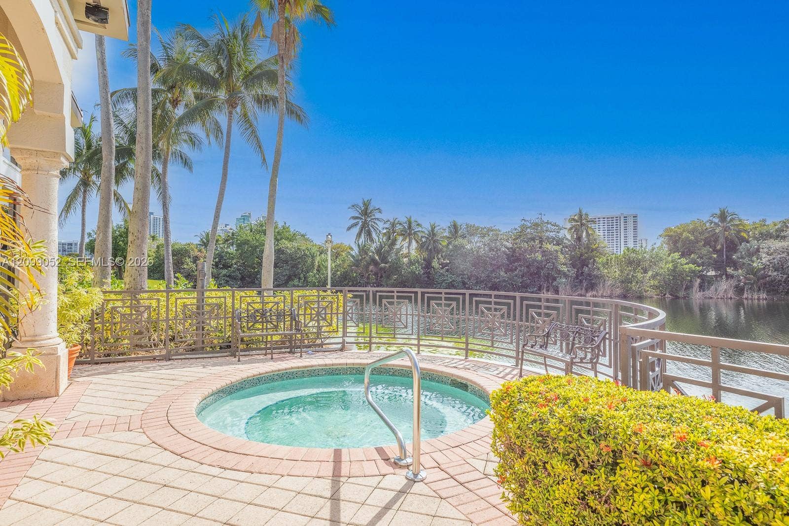 1516 Breakwater Terrace, Hollywood, FL 33019 Circular in-ground spa featuring a tiled interior and stainless steel handrail, surrounded by a paved deck, decorative metal railing, and manicured landscaping