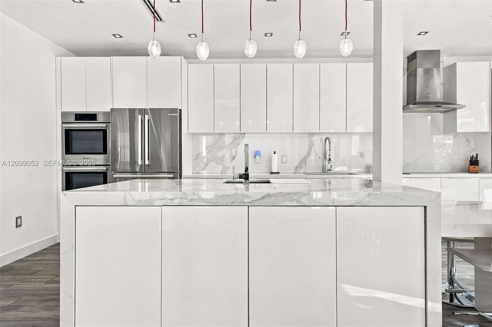 1516 Breakwater Terrace, Hollywood, FL 33019 Kitchen featuring high-gloss white cabinetry, a waterfall-edge stone island, stainless steel built-in double wall ovens, a coordinating range hood, and pendant lighting